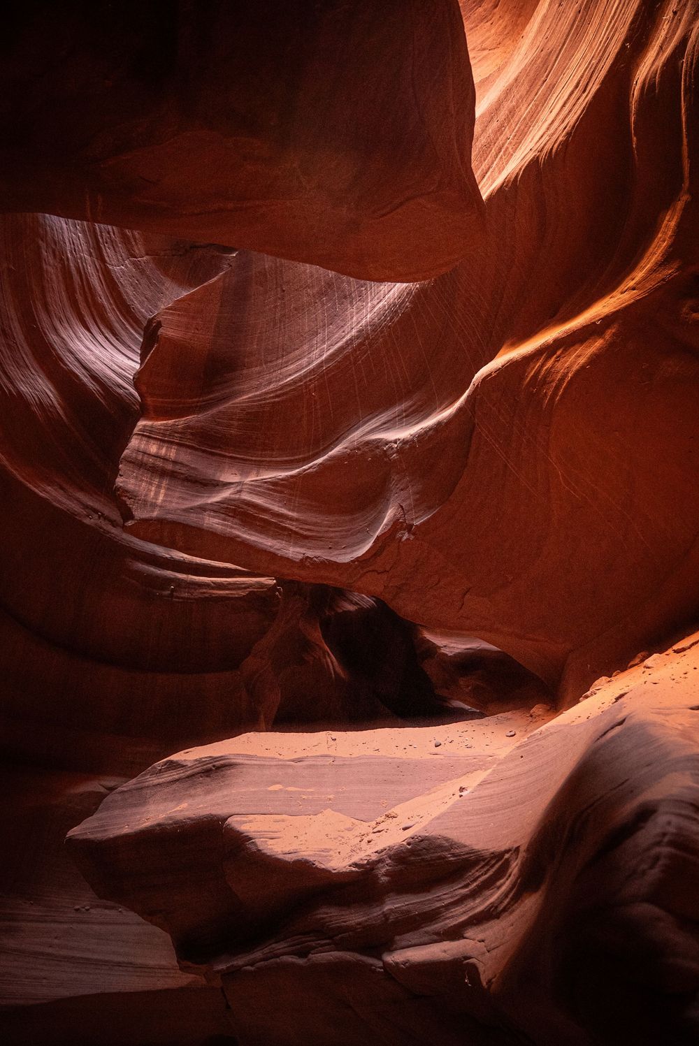 Antelope Canyon slot canyon interior with warm orange sandstone walls illuminated by natural light and sandy floor.