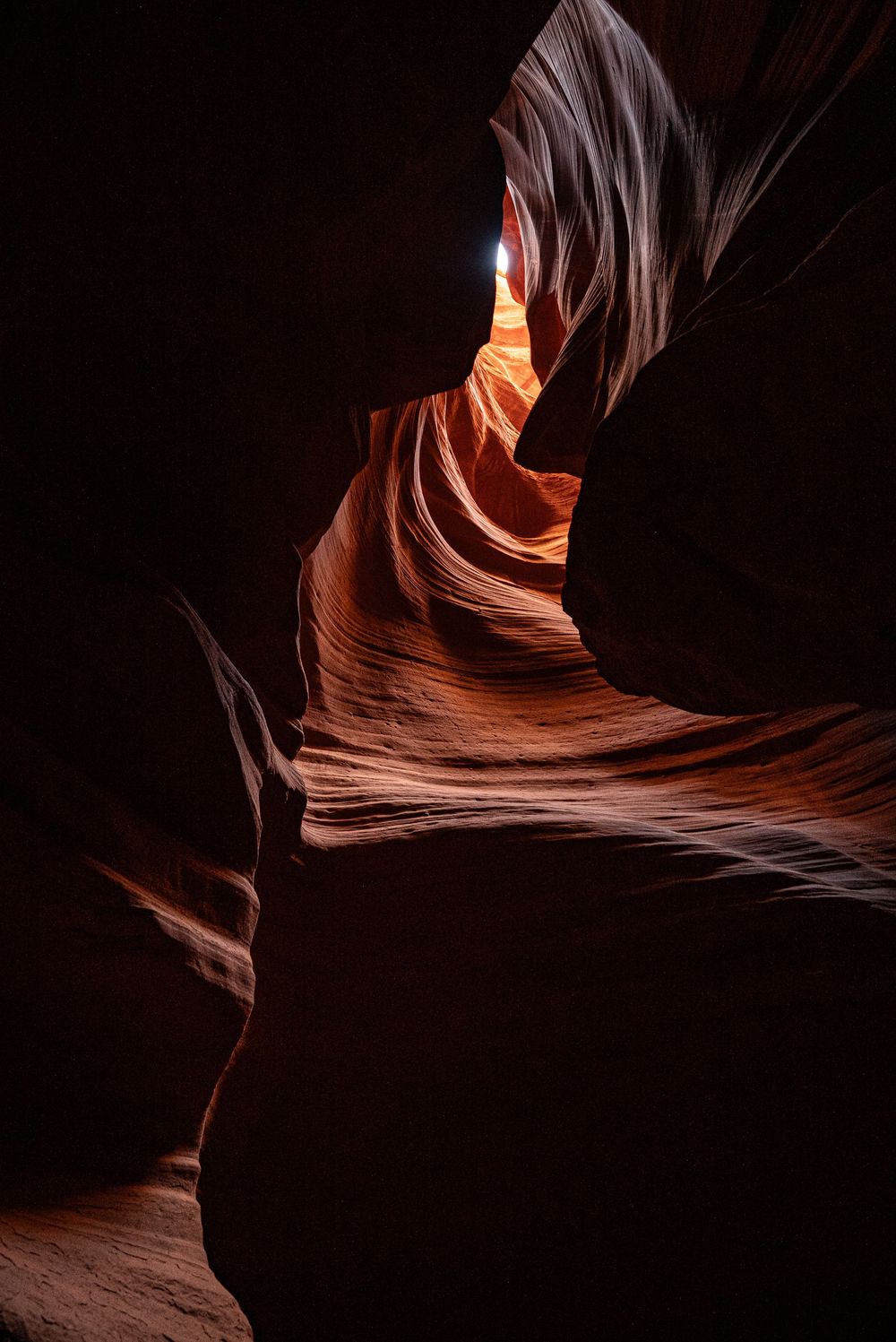 Dark dramatic Antelope Canyon slot canyon with glowing orange sandstone walls and single beam of light from above.