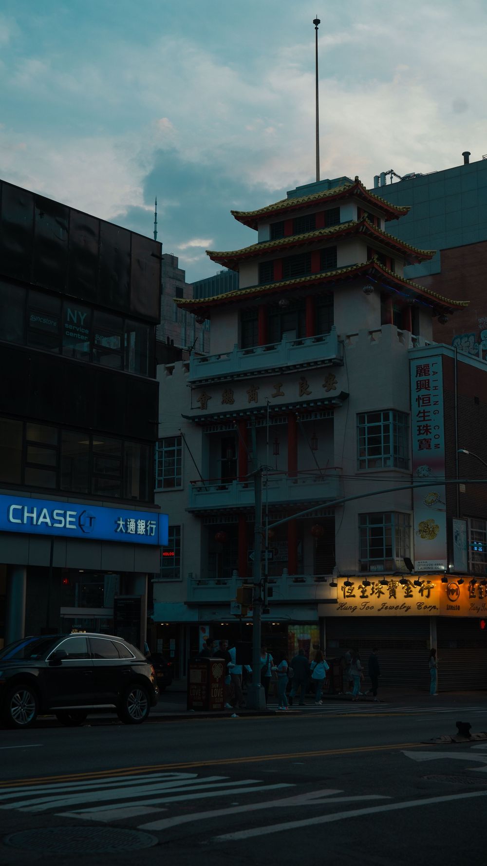 Chinatown street corner at dusk featuring a traditional pagoda-style building with Chinese signs and a Chase bank.
