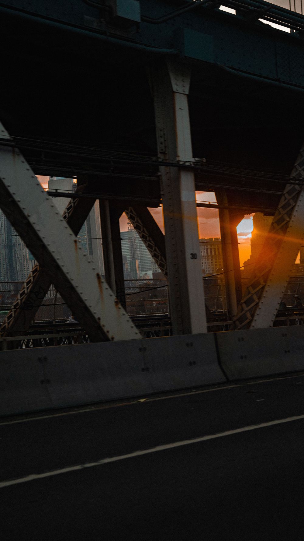 Urban bridge steel structure at sunset with golden light streaming through metal beams over empty road.