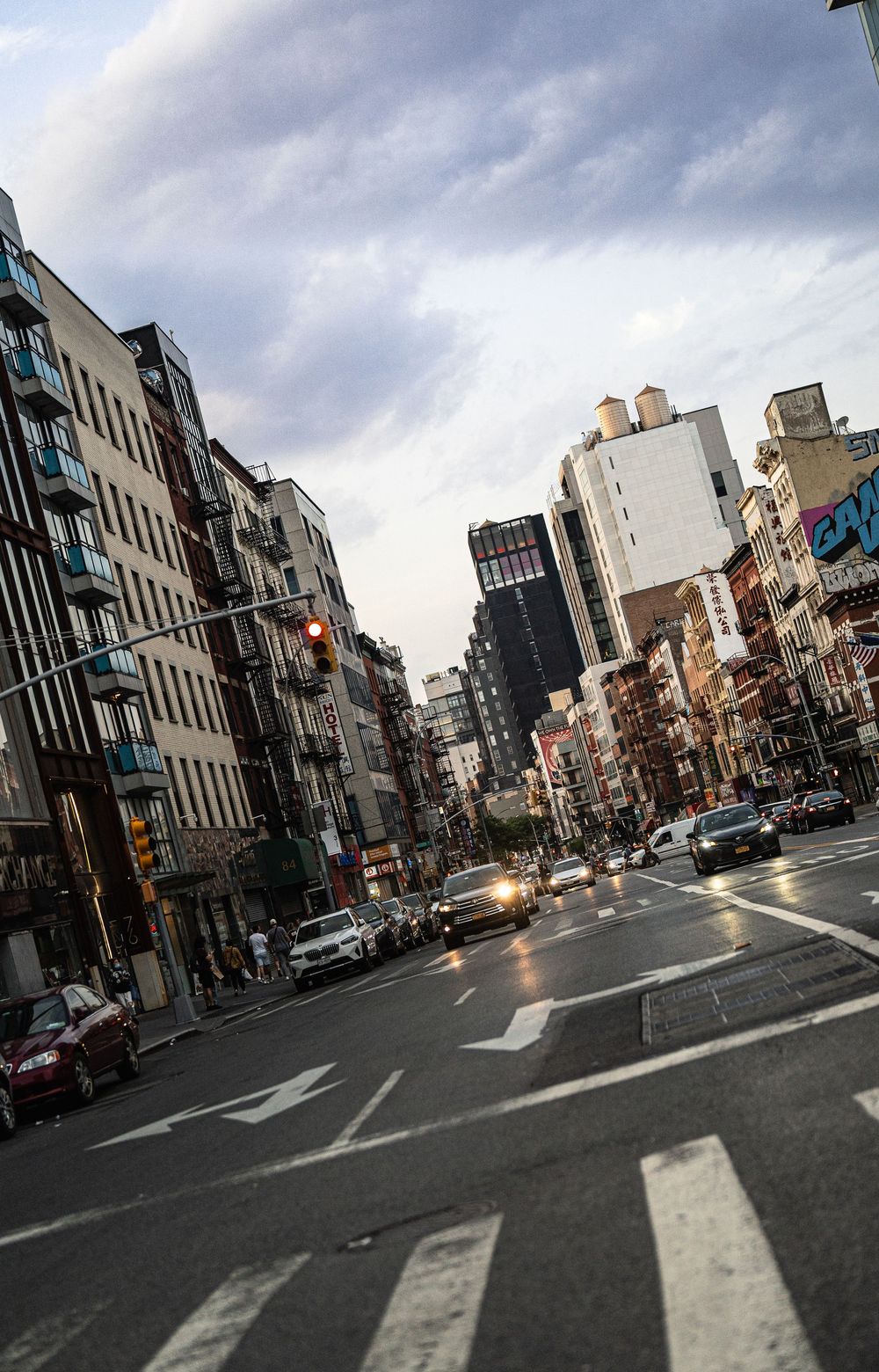 Busy urban intersection in New York City with yellow taxis, city buildings, and a red traffic light under a cloudy sky.