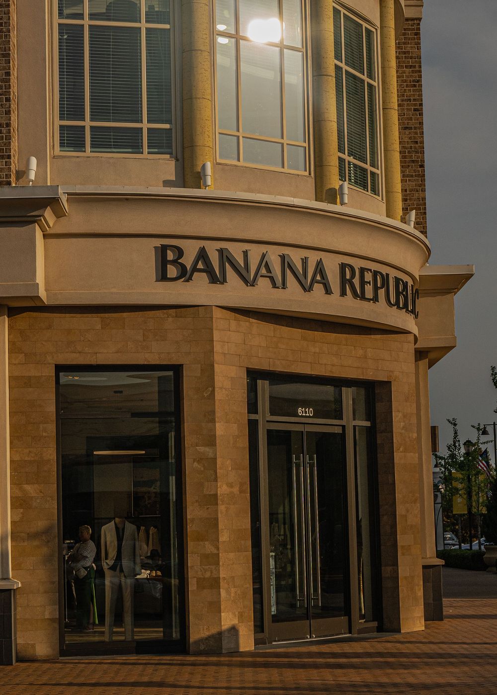 Exterior view of Banana Republic retail store with illuminated signage on curved brick building at dusk.
