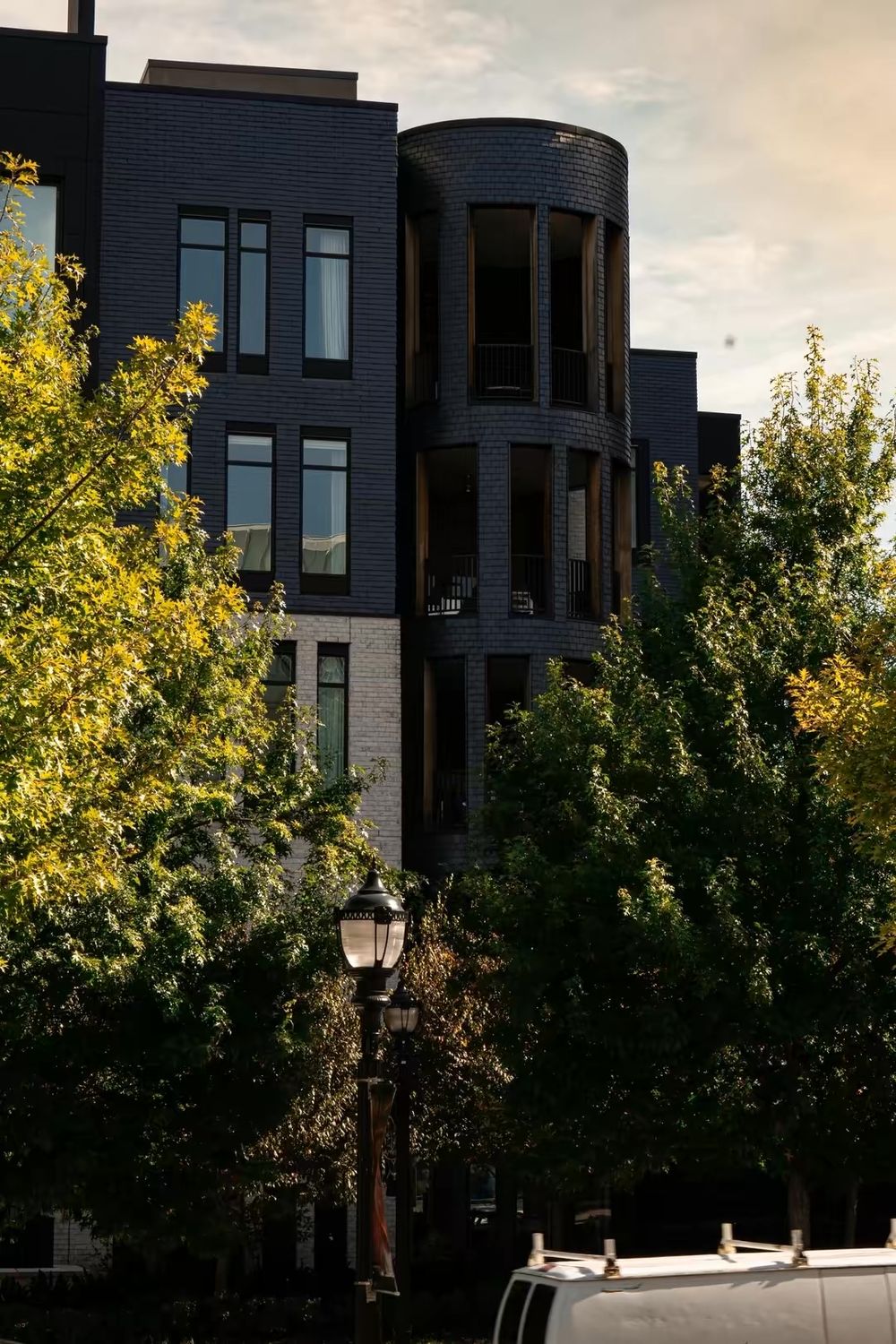 Dark brick building with cylindrical tower feature surrounded by autumn trees and a street lamp.