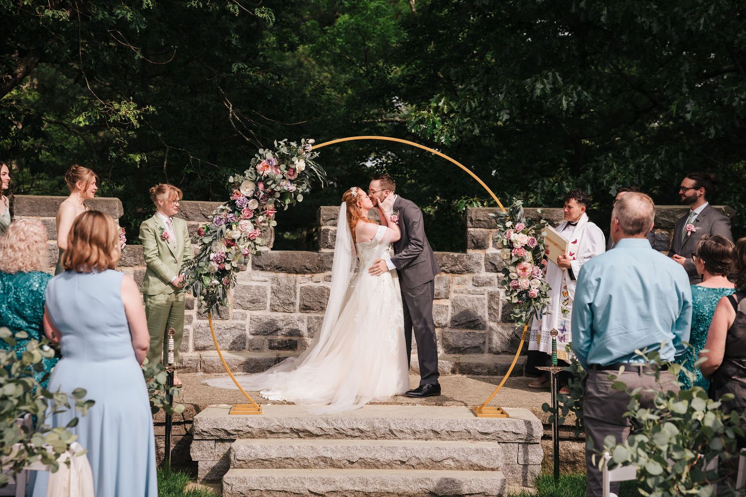 Bride and groom sharing their first kiss as a married couple under the gold floral arch at the ceremony.