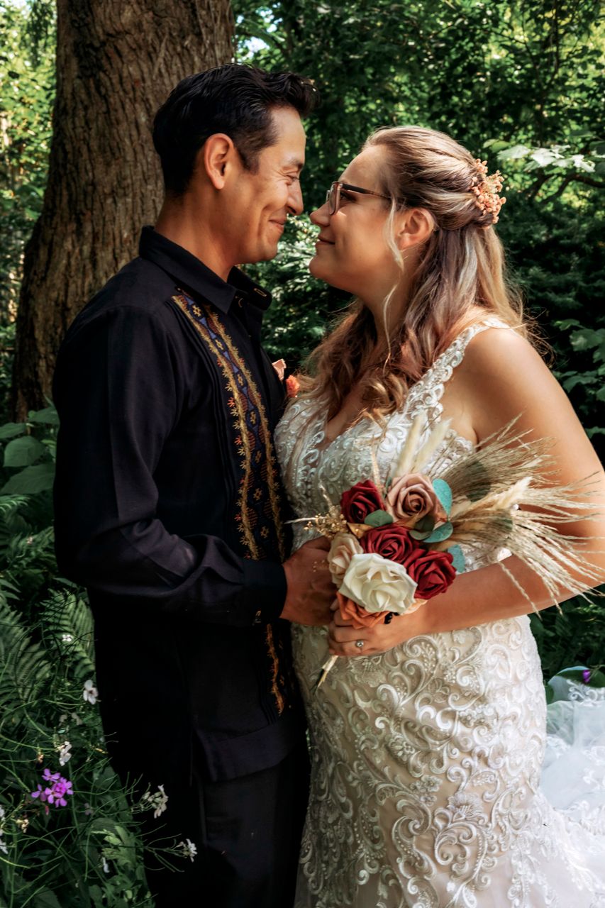 A bride and groom share a romantic moment in a lush forest setting, with the bride holding a colorful bouquet.