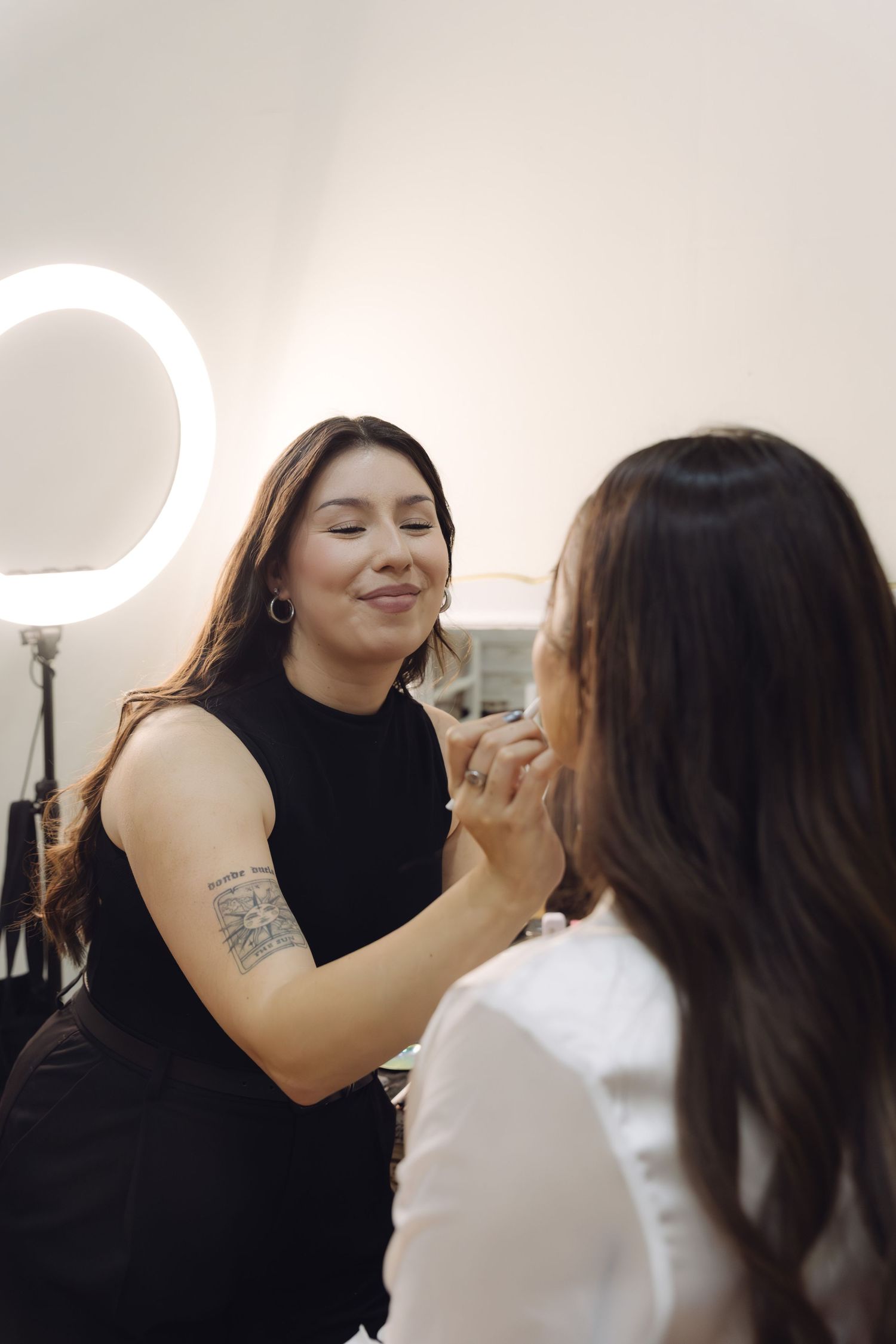 Professional makeup artist applying makeup to bride in white robe under ring light in beauty studio.