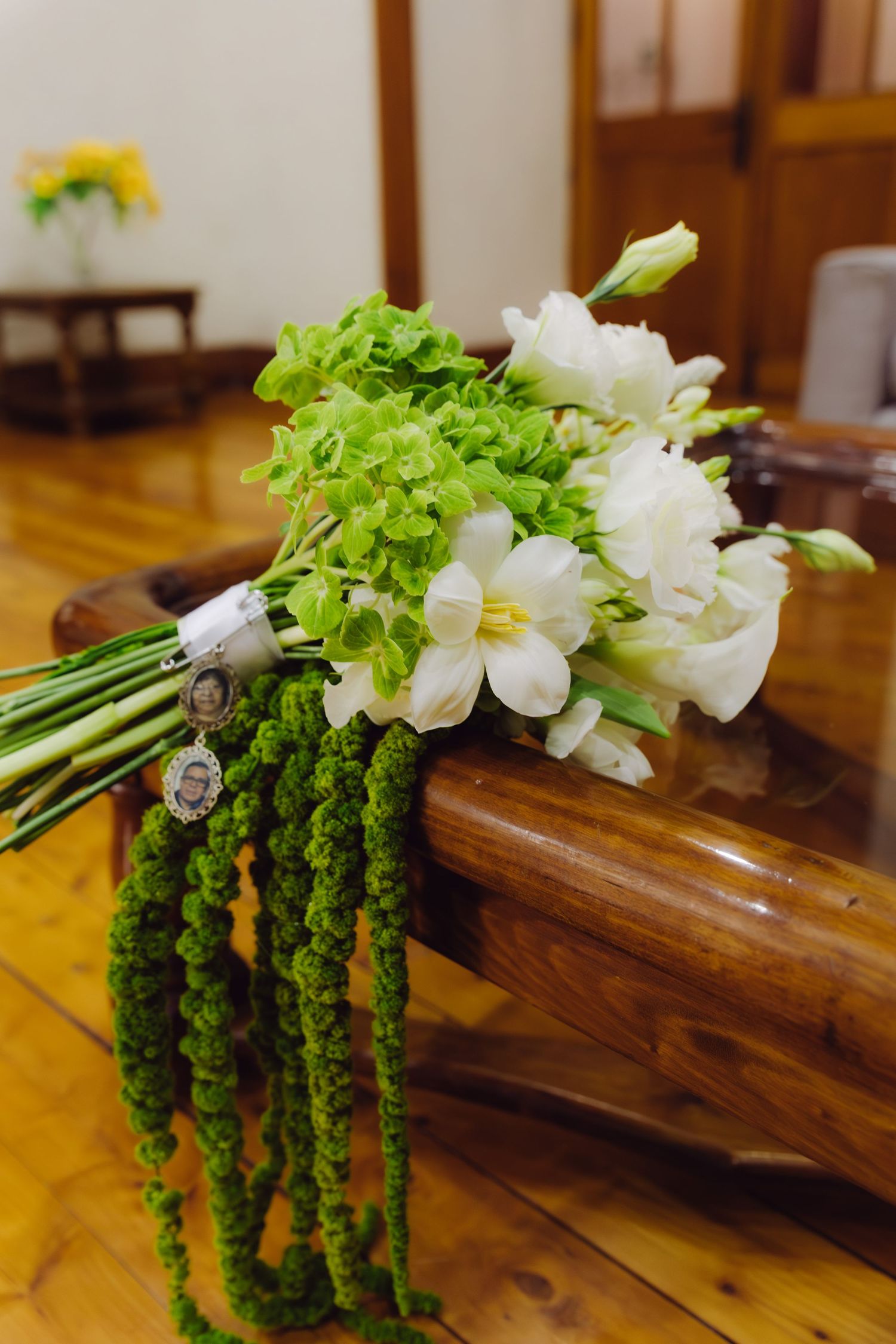 Elegant bridal bouquet of white freesias and green flowers with memorial photo charms on wooden bench.