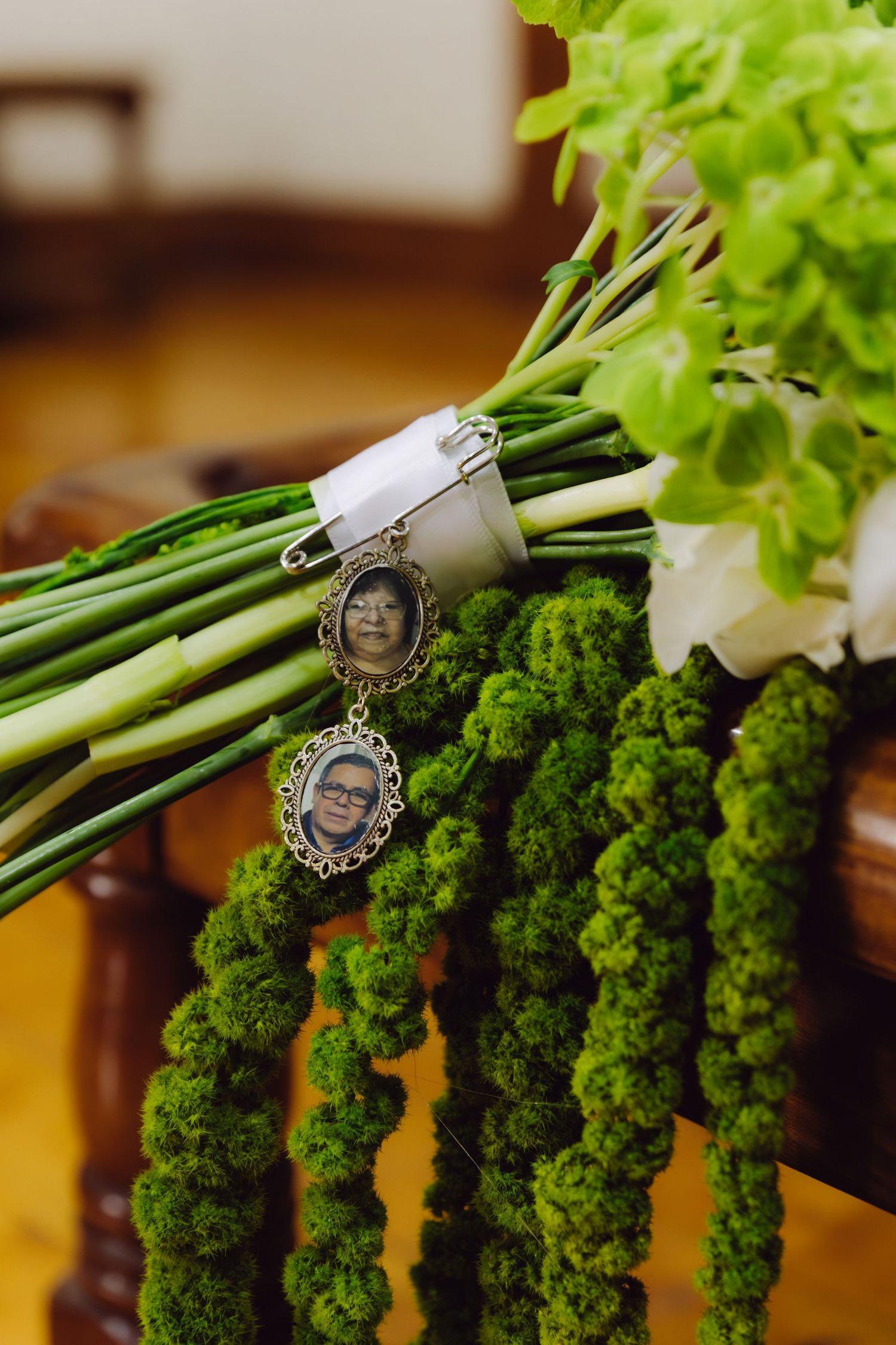 Close-up of bridal bouquet with sentimental memorial photo lockets hanging from green floral arrangement.