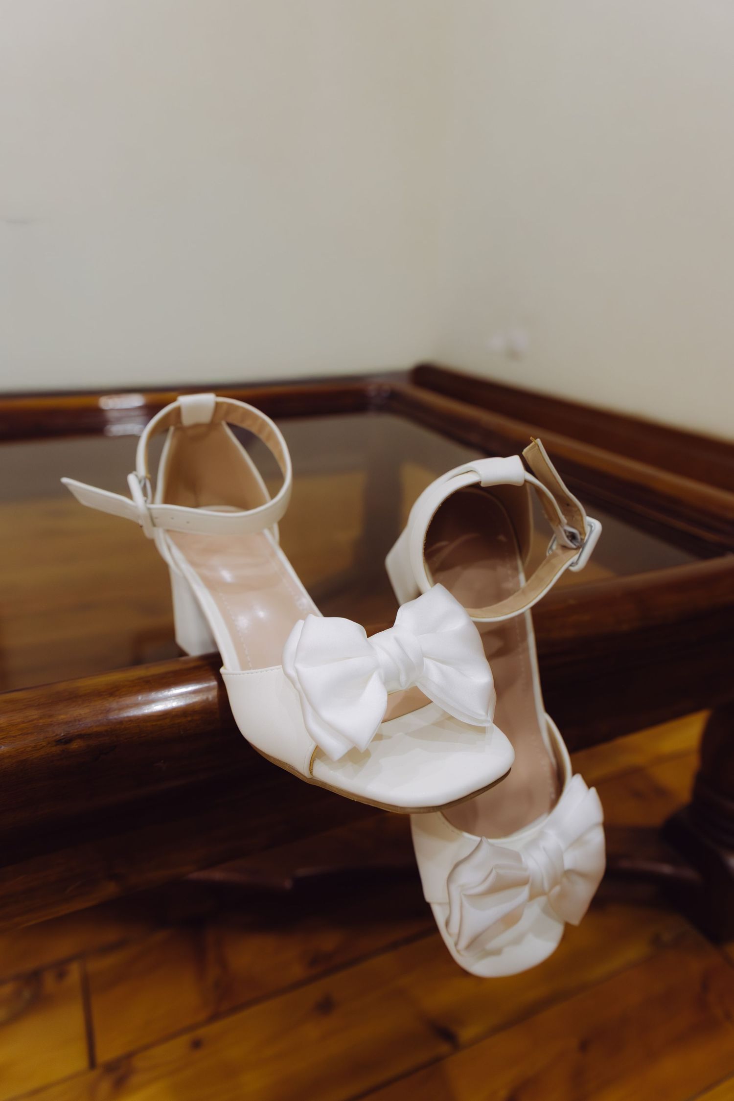 White block heel bridal sandals with bow detail displayed on wooden table for wedding day.