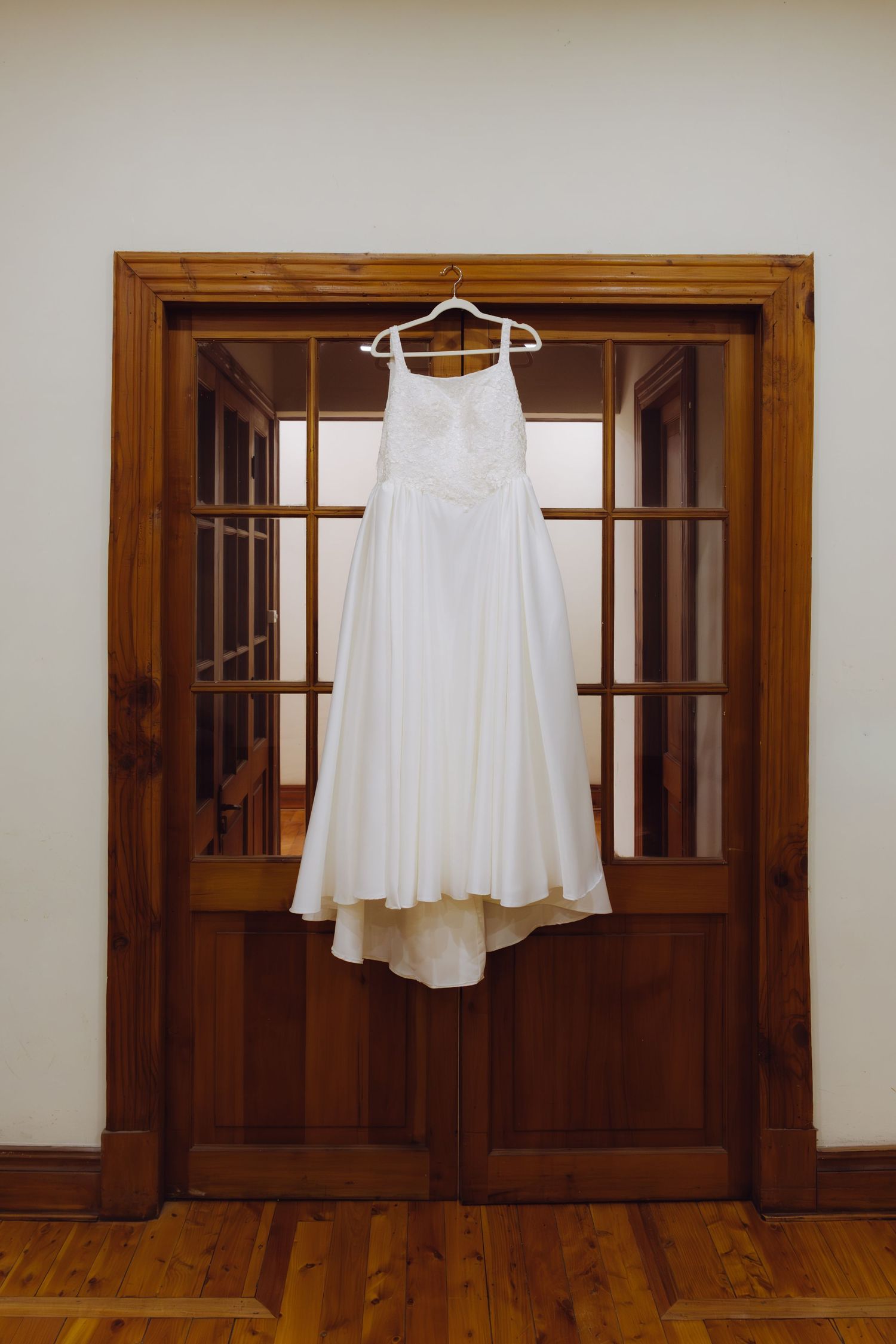 Elegant white A-line wedding dress hanging on wooden French doors in preparation for ceremony.