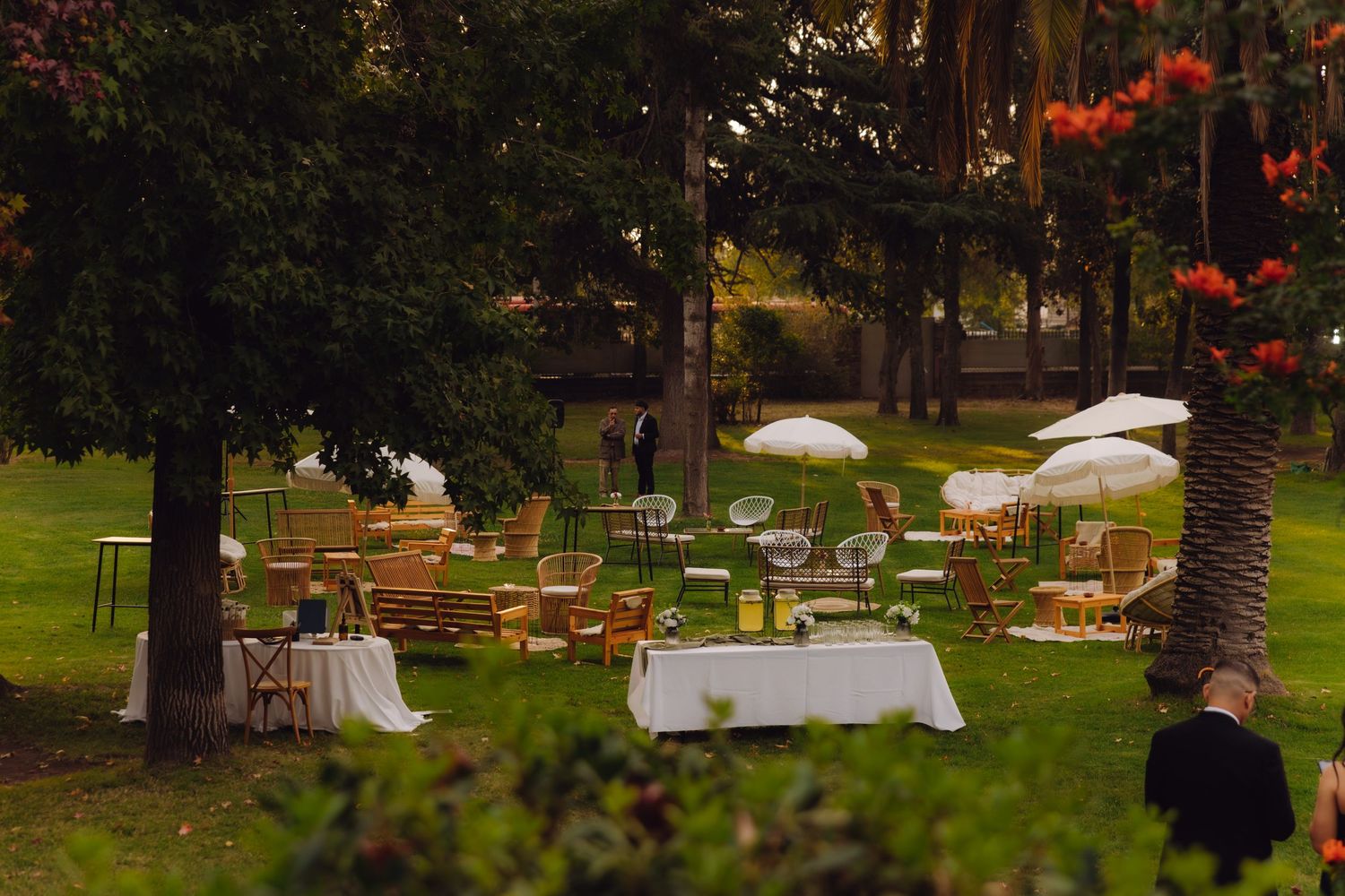 Romantic outdoor wedding reception setup with tables, umbrellas, and string lights in lush garden at dusk.