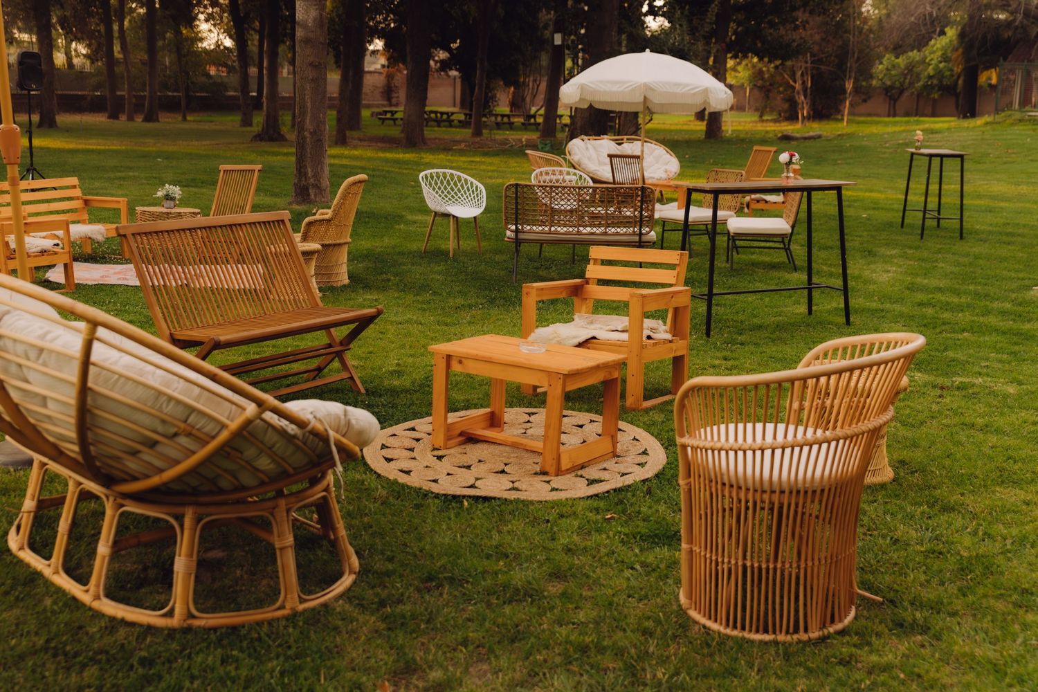 Elegant outdoor wedding lounge area with rattan and wooden chairs arranged on green grass.