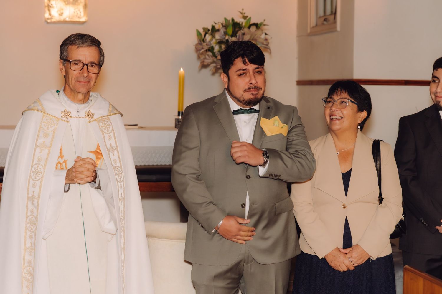 Groom in gray suit with yellow boutonniere stands at church altar during wedding ceremony.