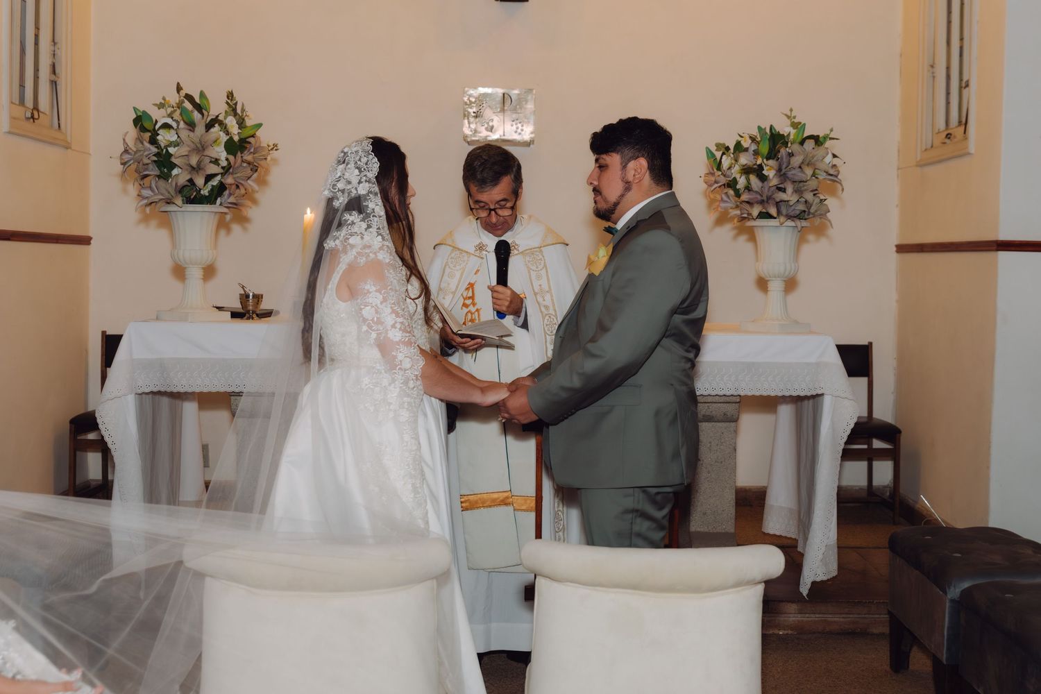 Groom places ring on brides hand as officiant presides over wedding ceremony at church altar.