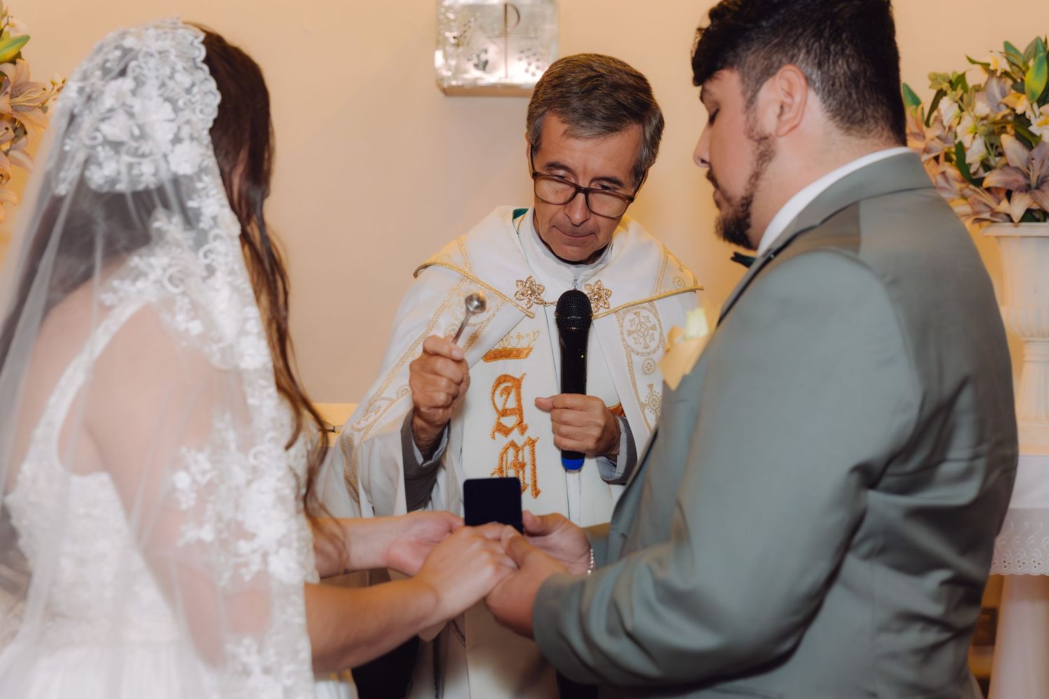 Priest officiates wedding ceremony as bride and groom exchange rings at the altar.