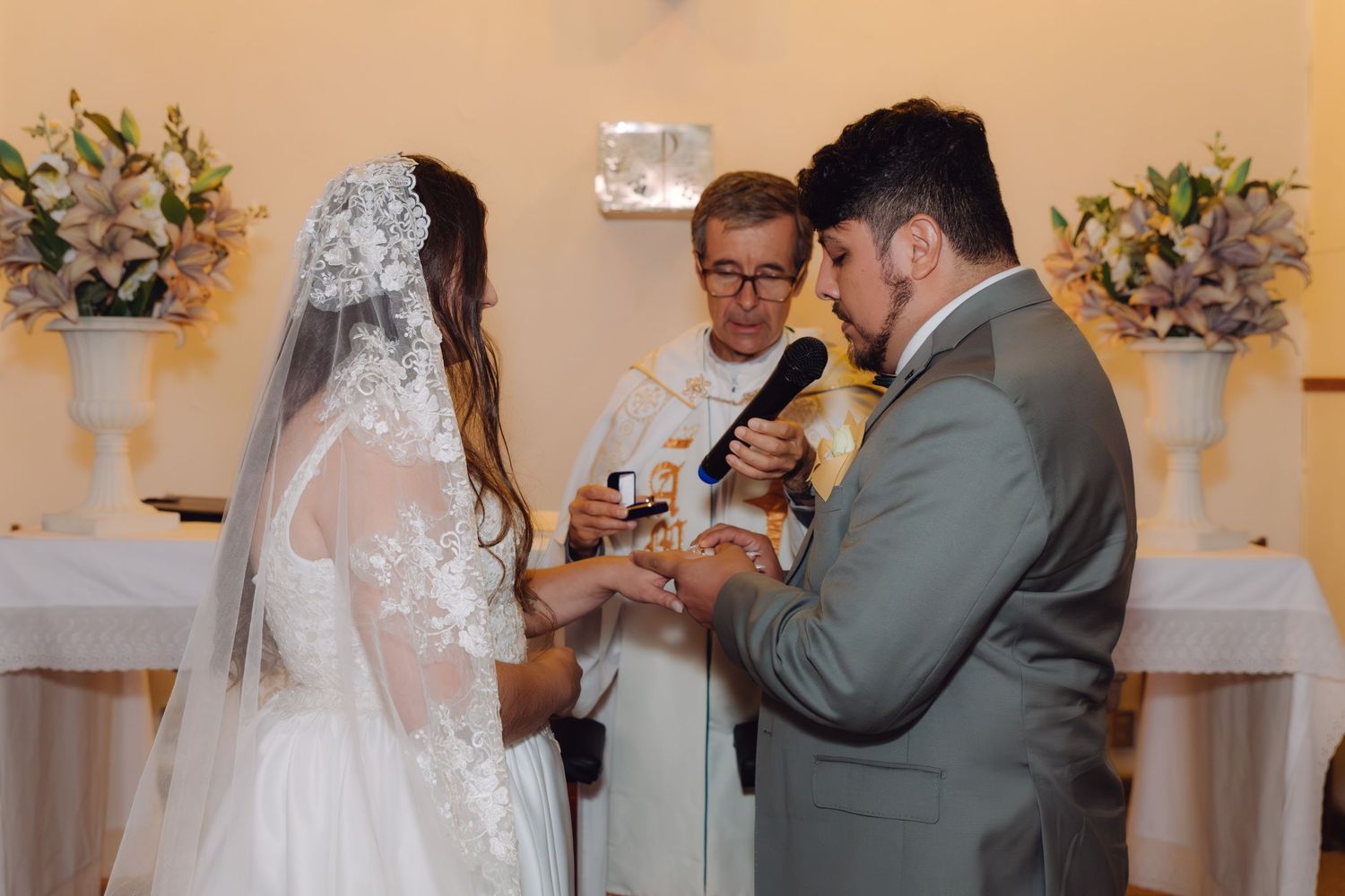 Bride and groom exchange rings during religious wedding ceremony with officiant.
