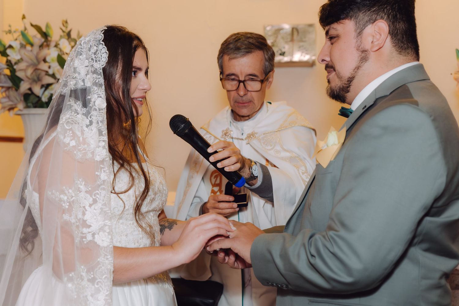 Couple exchanges wedding rings during Catholic church ceremony with priest present.