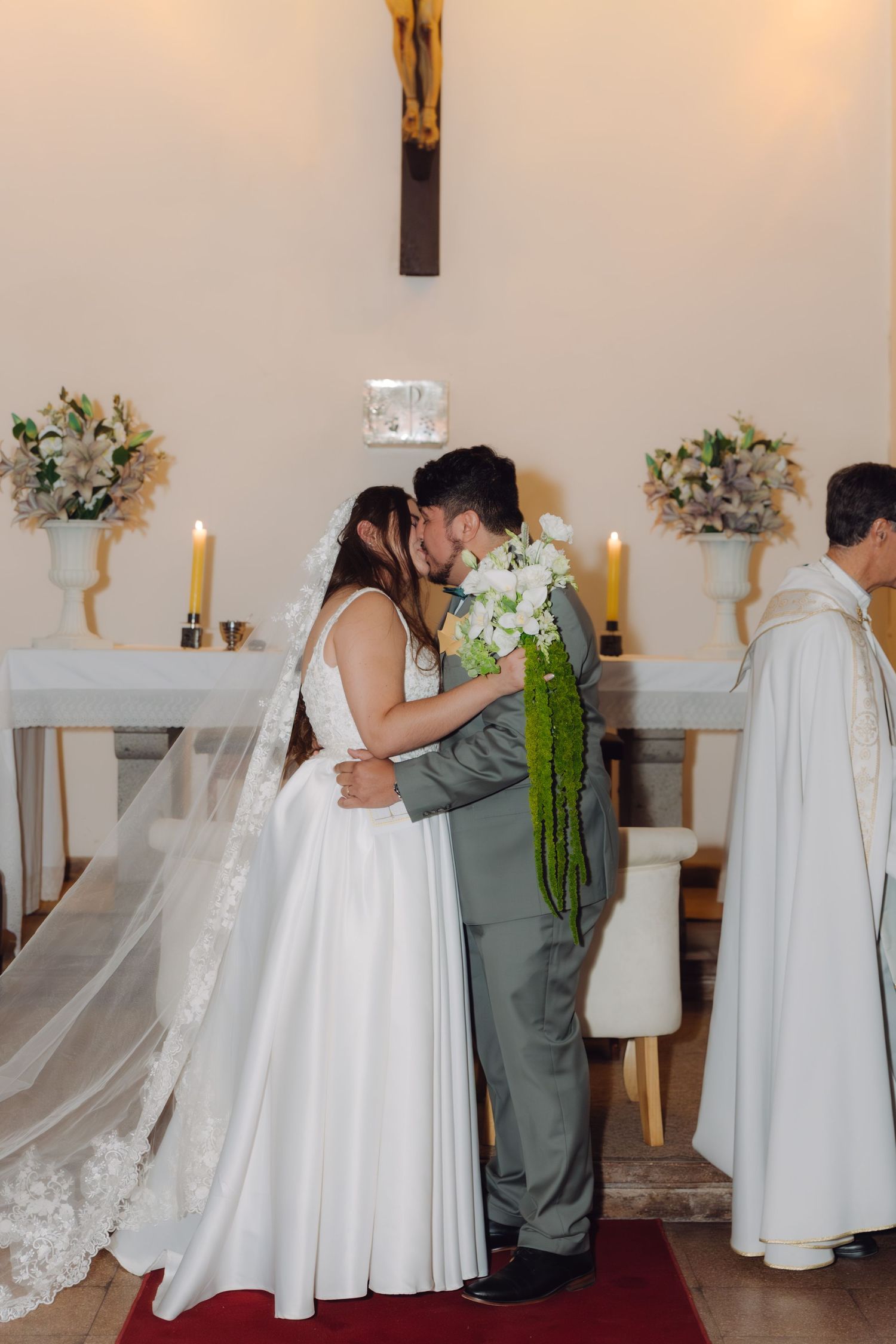 Newlyweds share first kiss at church altar with crucifix and candles.