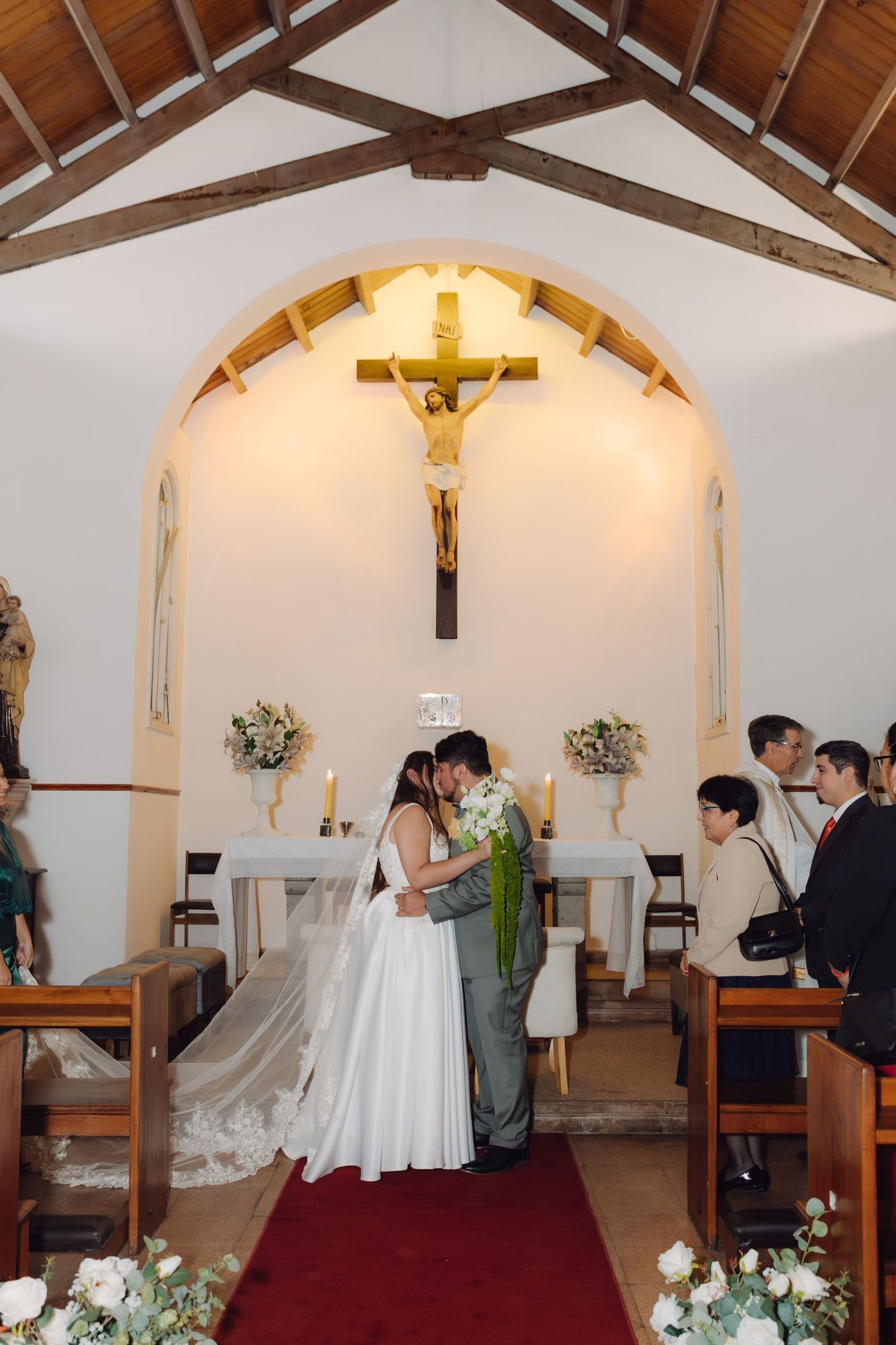 Bride and groom kiss at altar of small Catholic chapel during wedding.