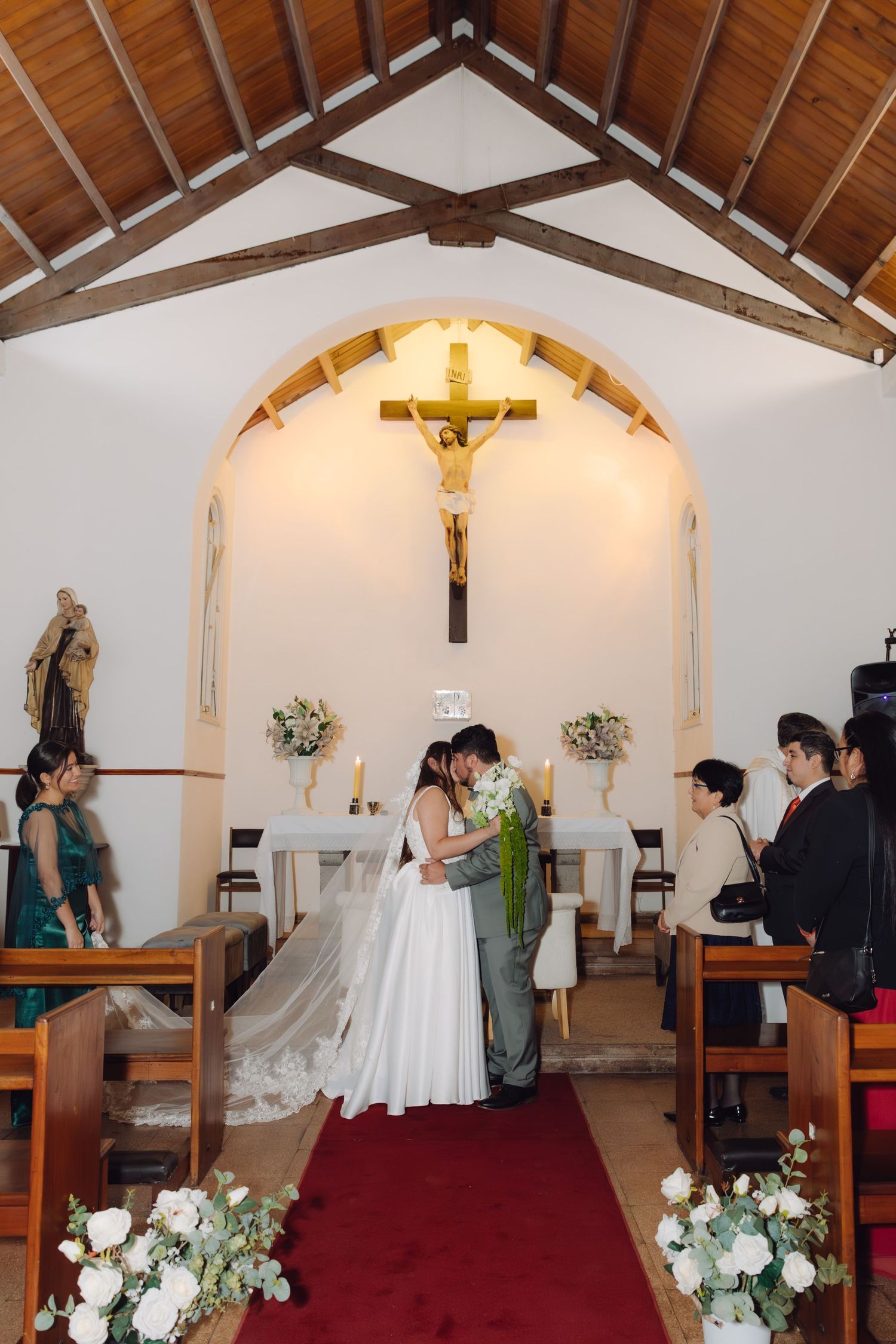 Bride and groom share a romantic kiss at the altar of a small white Catholic chapel during their wedding ceremony.