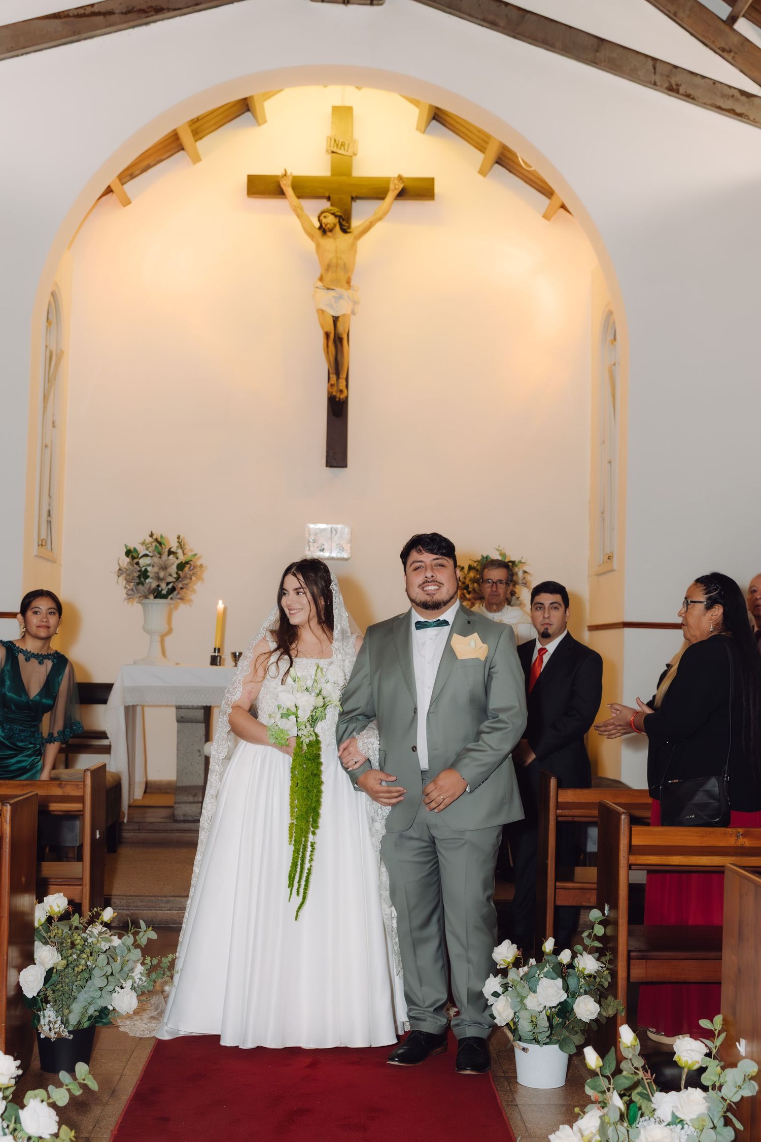 Newlyweds walk down the red carpet aisle of a charming white chapel after their wedding ceremony.