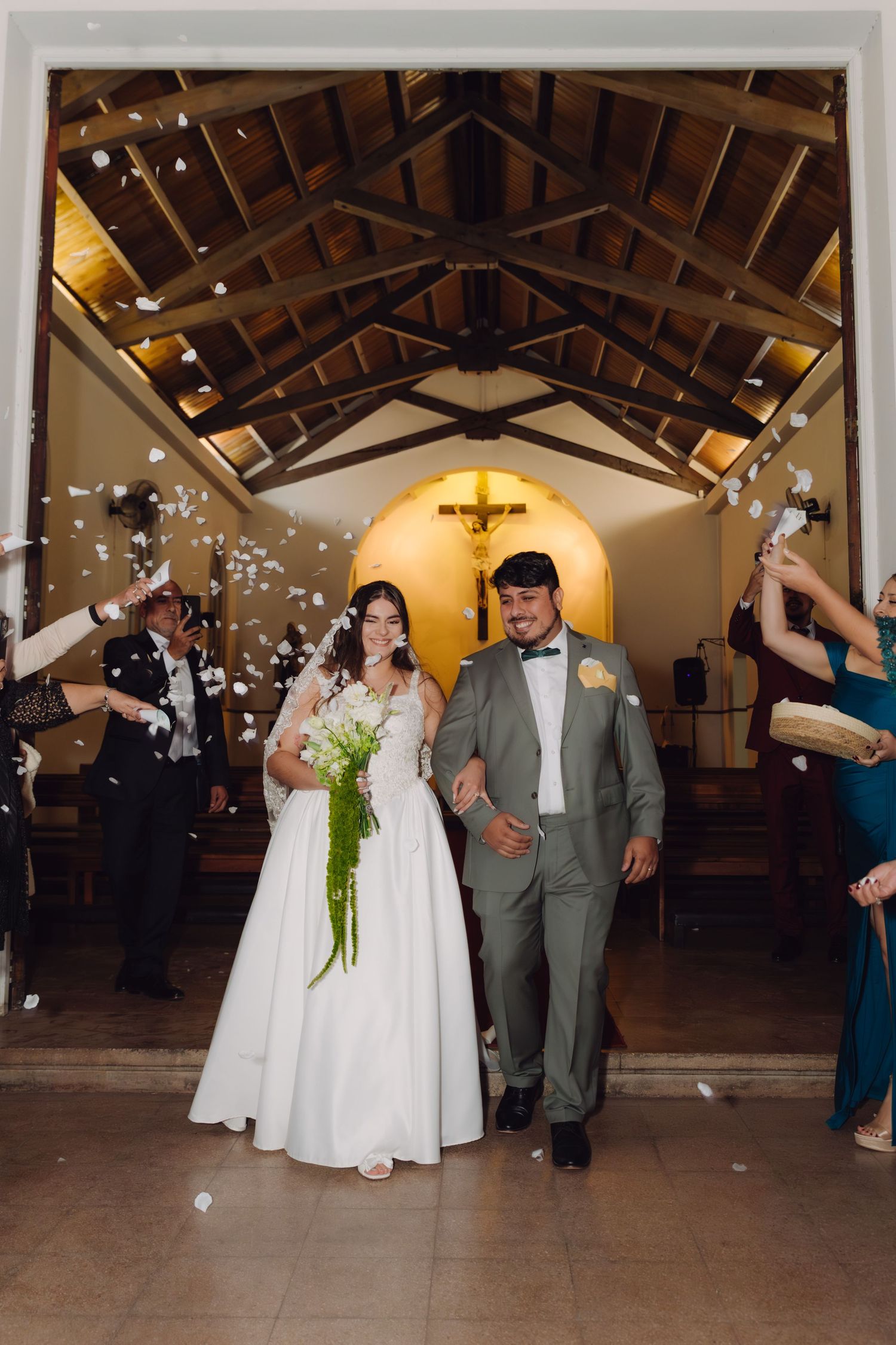 Joyful newlyweds exit a Catholic church as guests shower them with white flower petals in celebration.