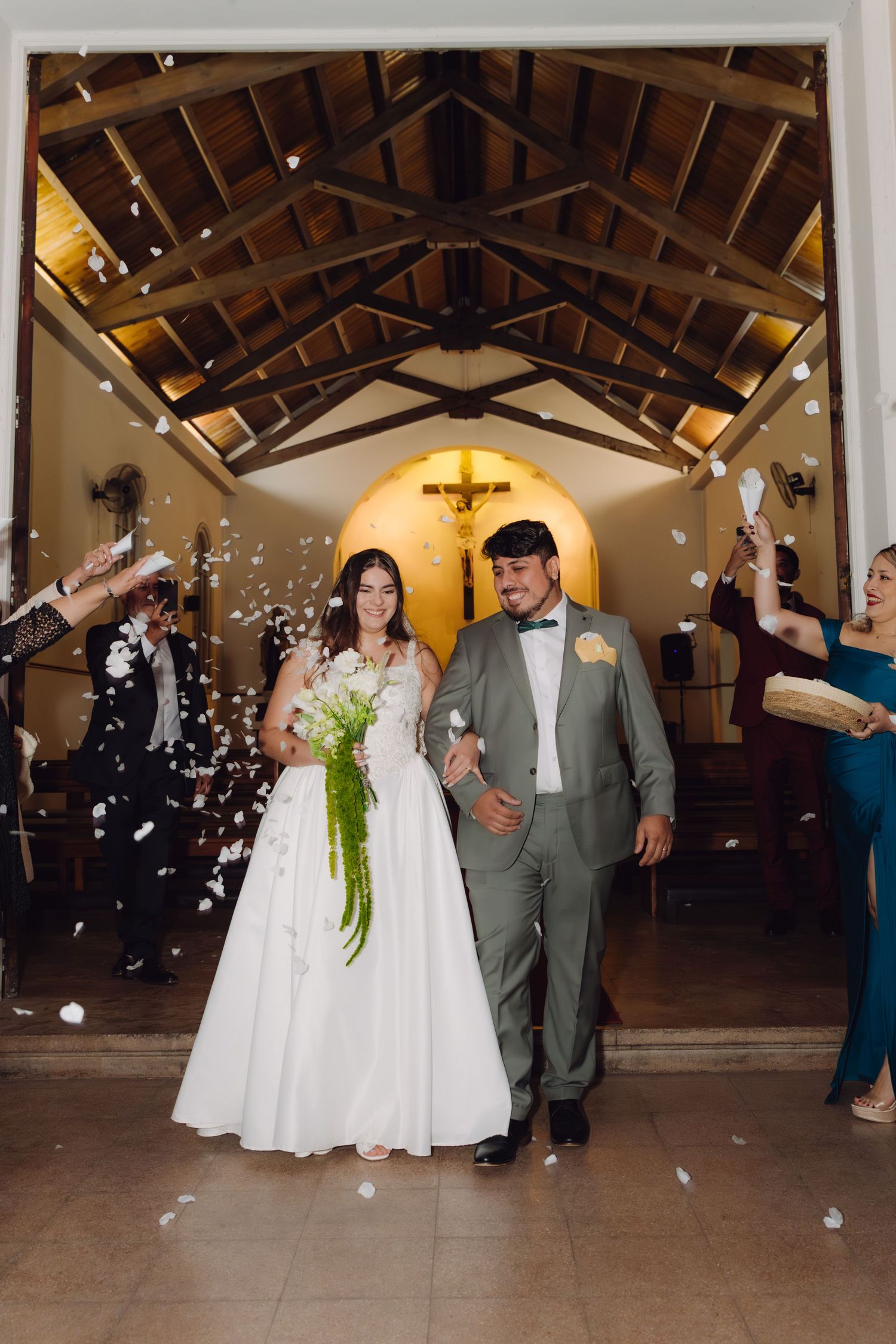 Bride and groom walk arm in arm through a confetti of white petals as guests celebrate their exit.