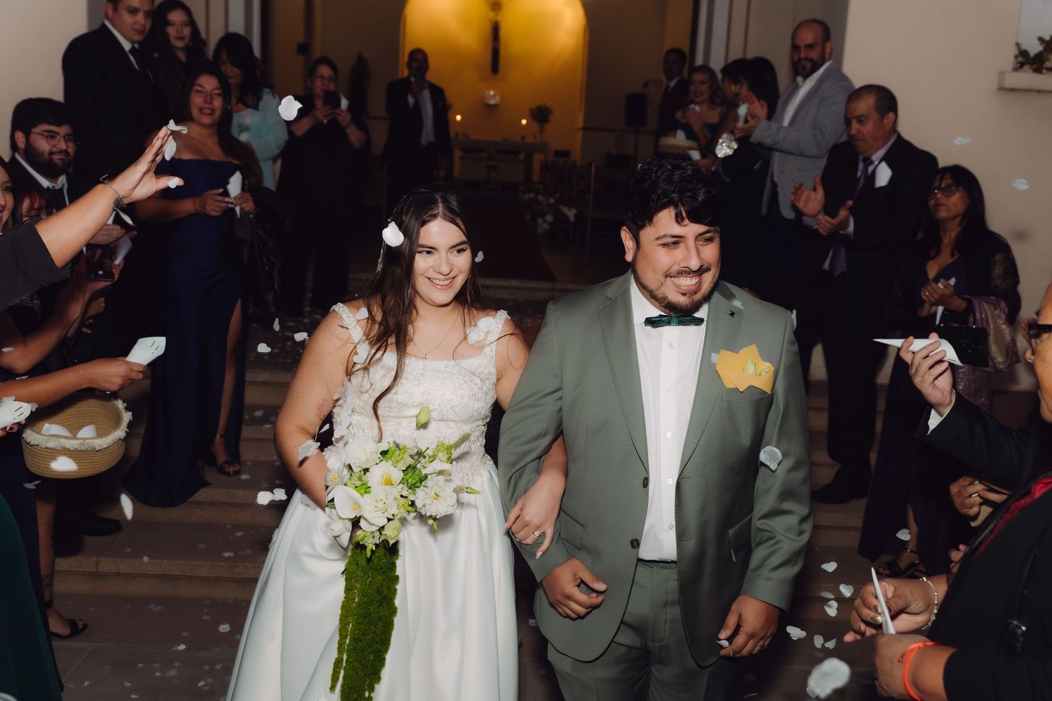 Smiling newlyweds walk through a crowd of cheering guests after their wedding ceremony at night.