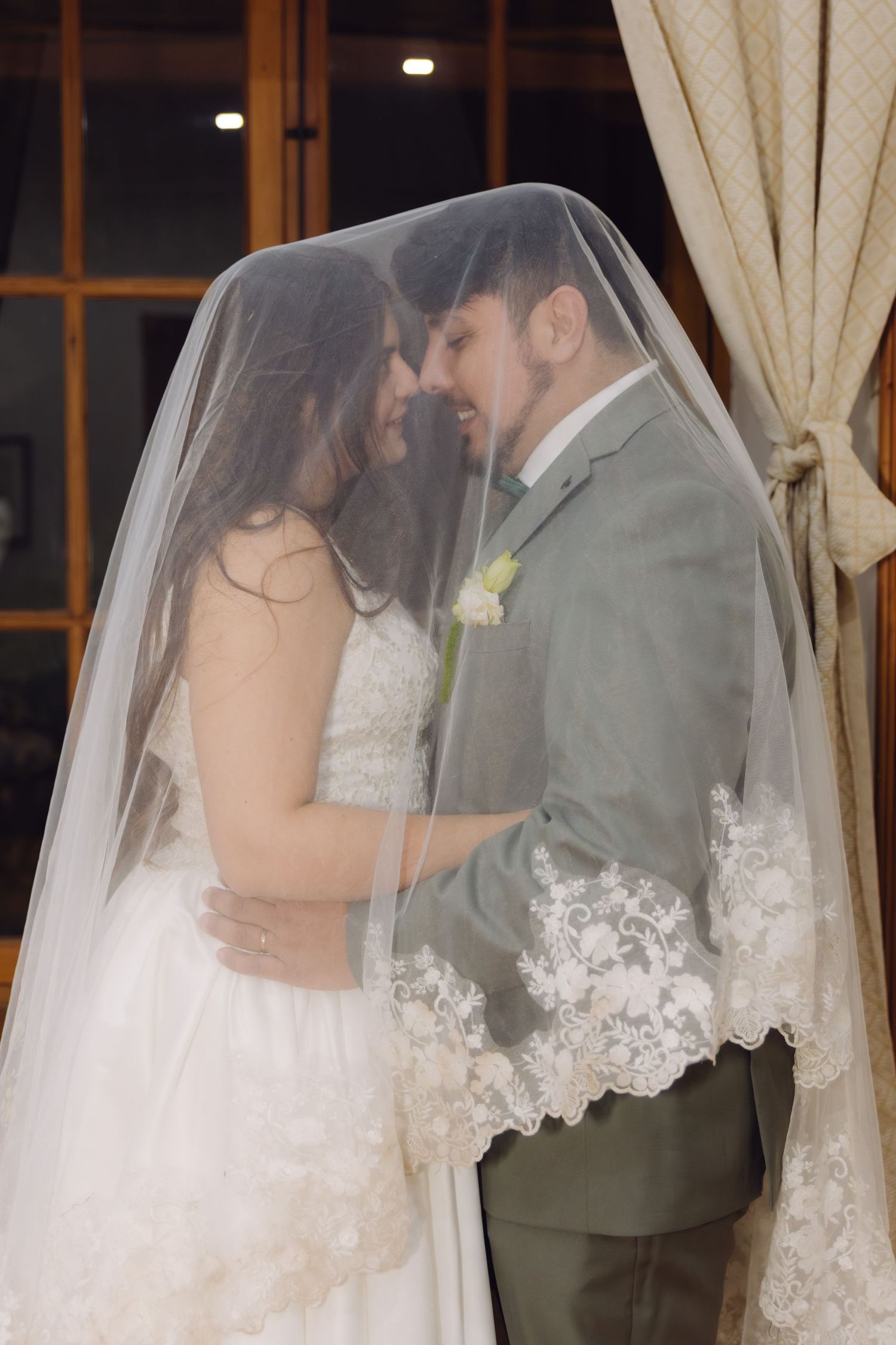 Bride and groom share a romantic moment together under the bride's lace-trimmed wedding veil.