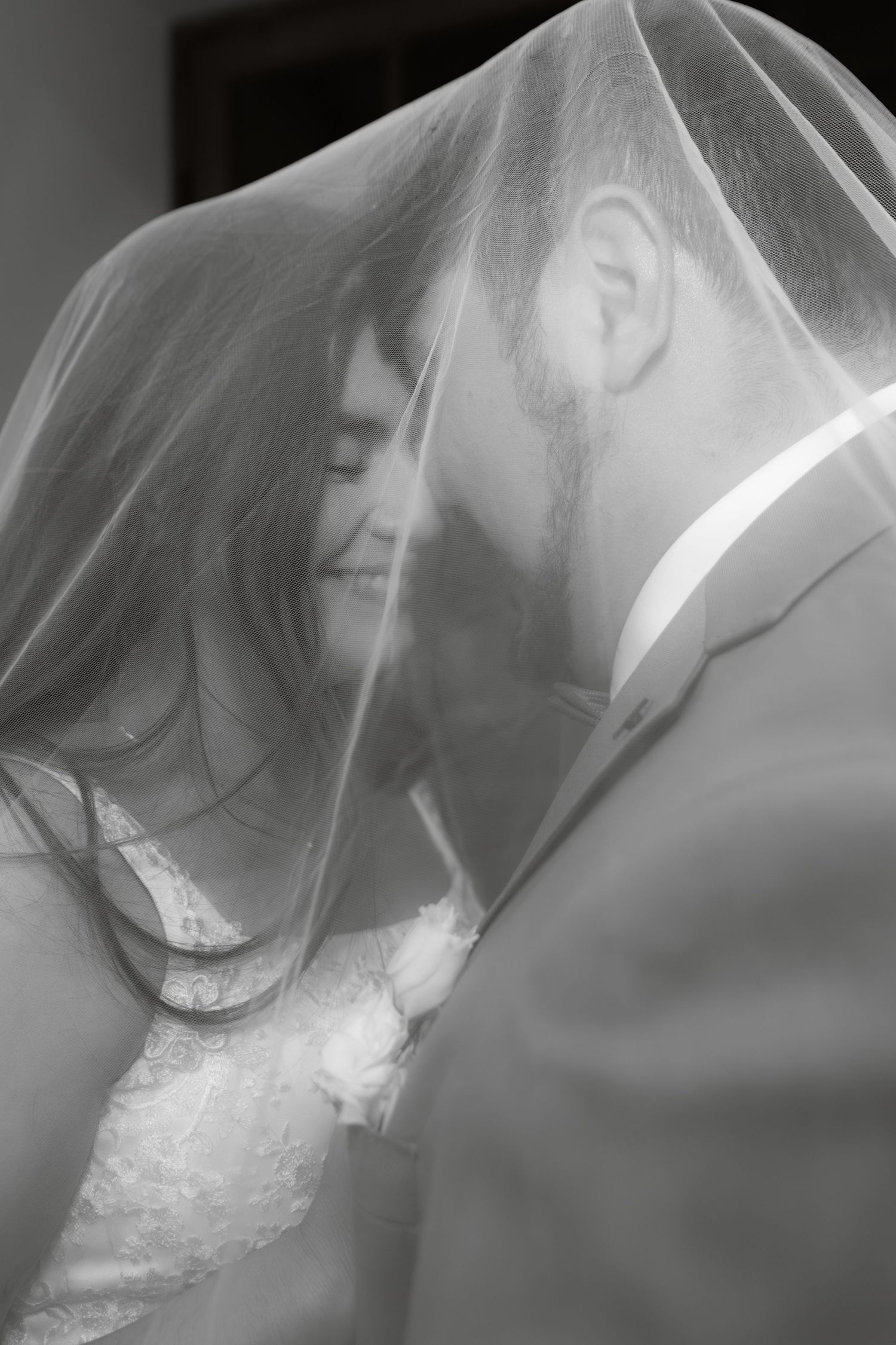 Black and white photo of a smiling bride and groom sharing an intimate moment beneath the wedding veil.