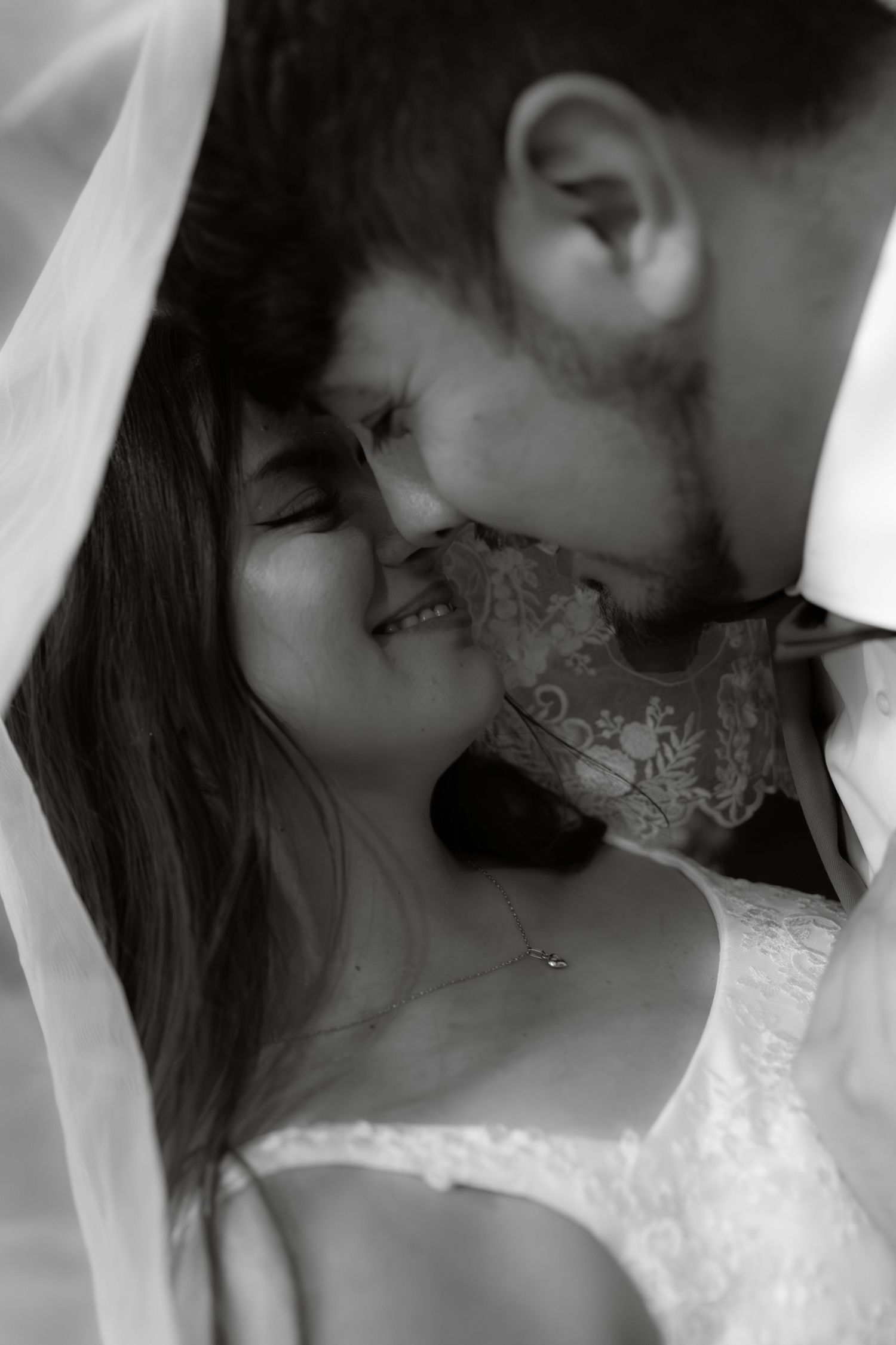 Romantic black and white close-up of a laughing bride and groom sharing a tender moment under her veil.
