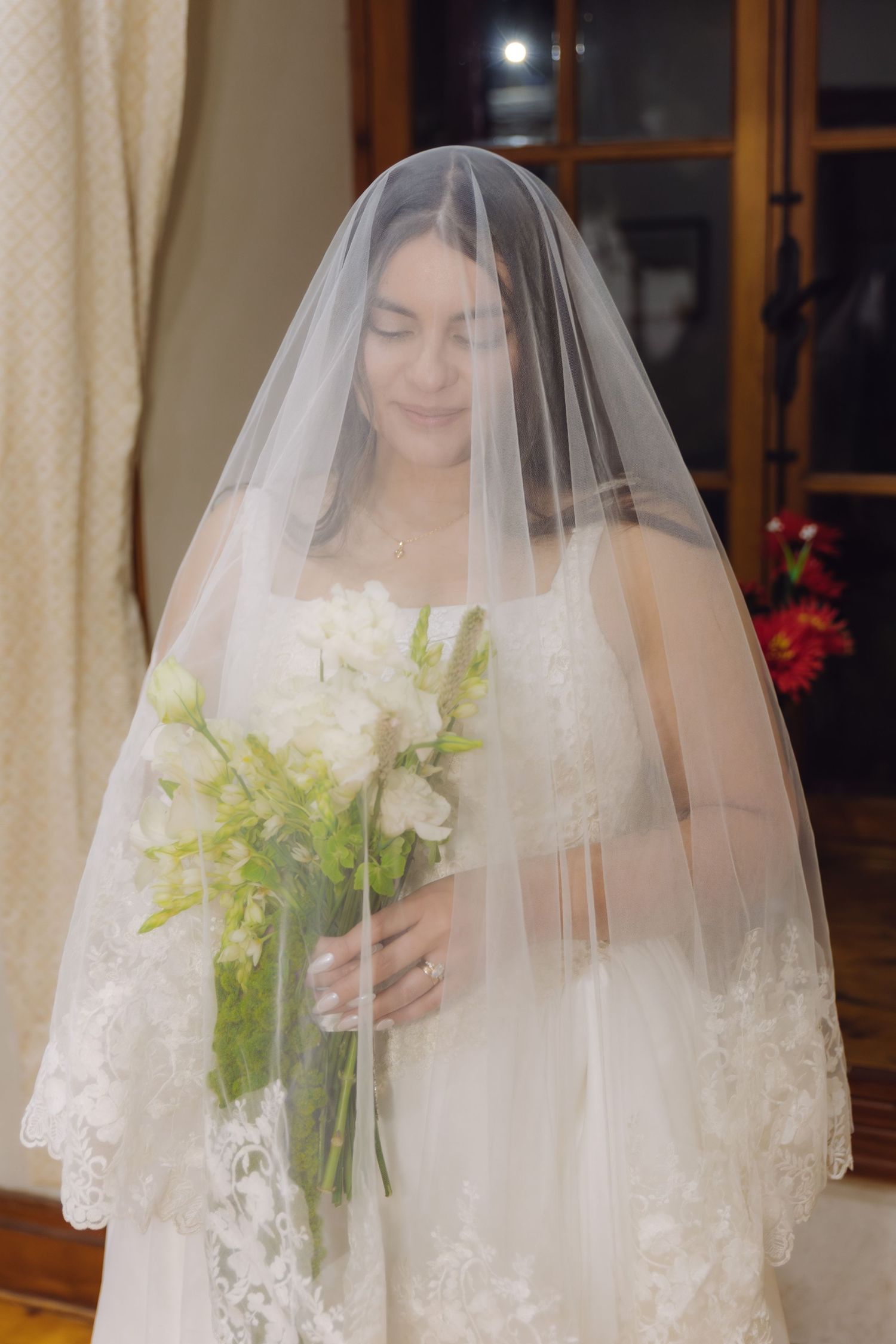 Bride in white lace wedding dress holds a bouquet of white flowers under her veil.