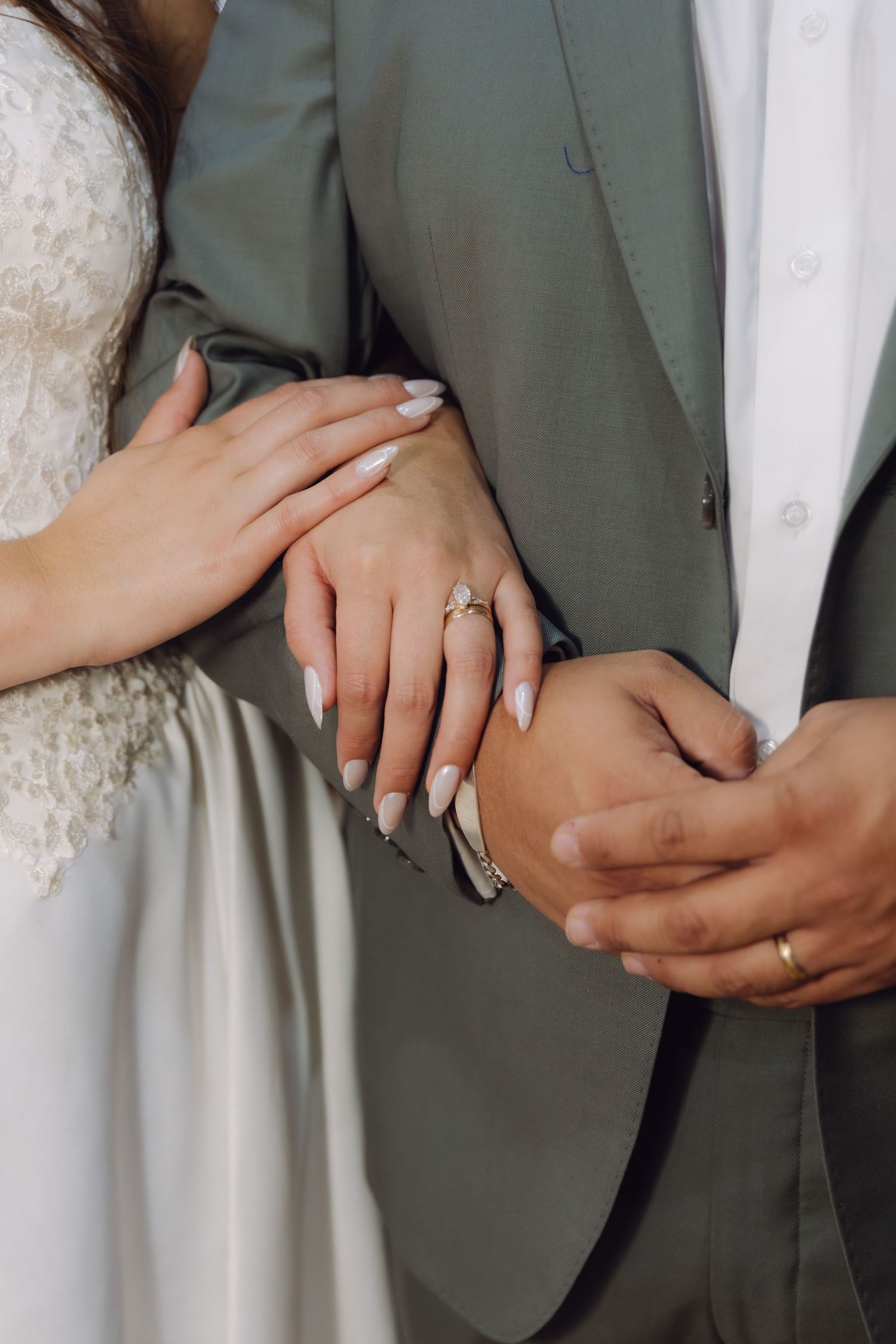 Close-up of bride and groom holding hands showing wedding rings in elegant attire.