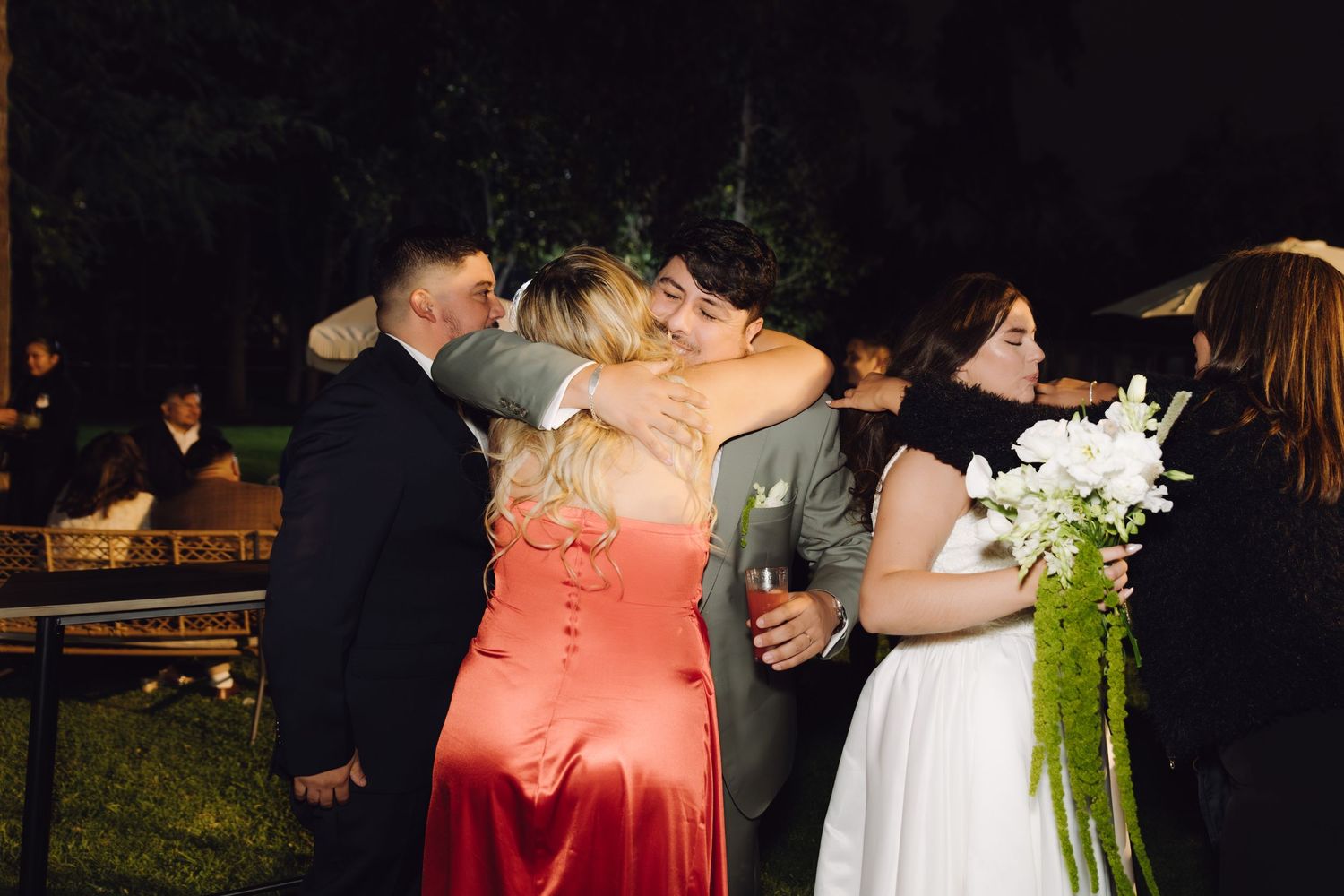 Wedding guests embrace and celebrate at an elegant outdoor nighttime reception ceremony.