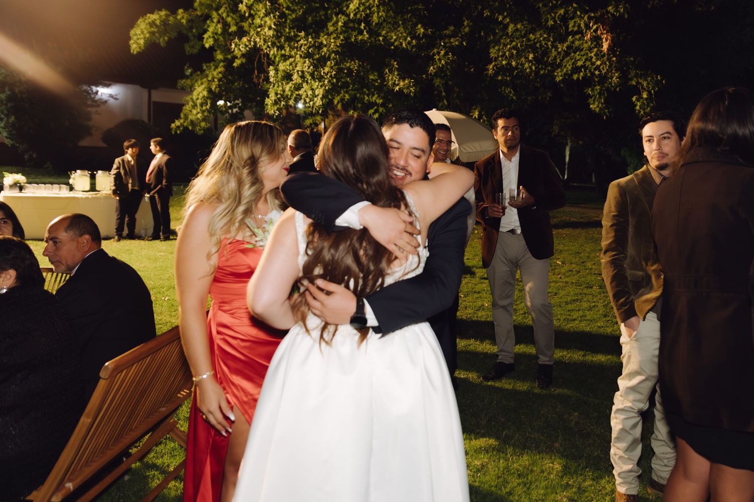 Bride and groom share joyful embraces with guests at elegant outdoor evening wedding reception.