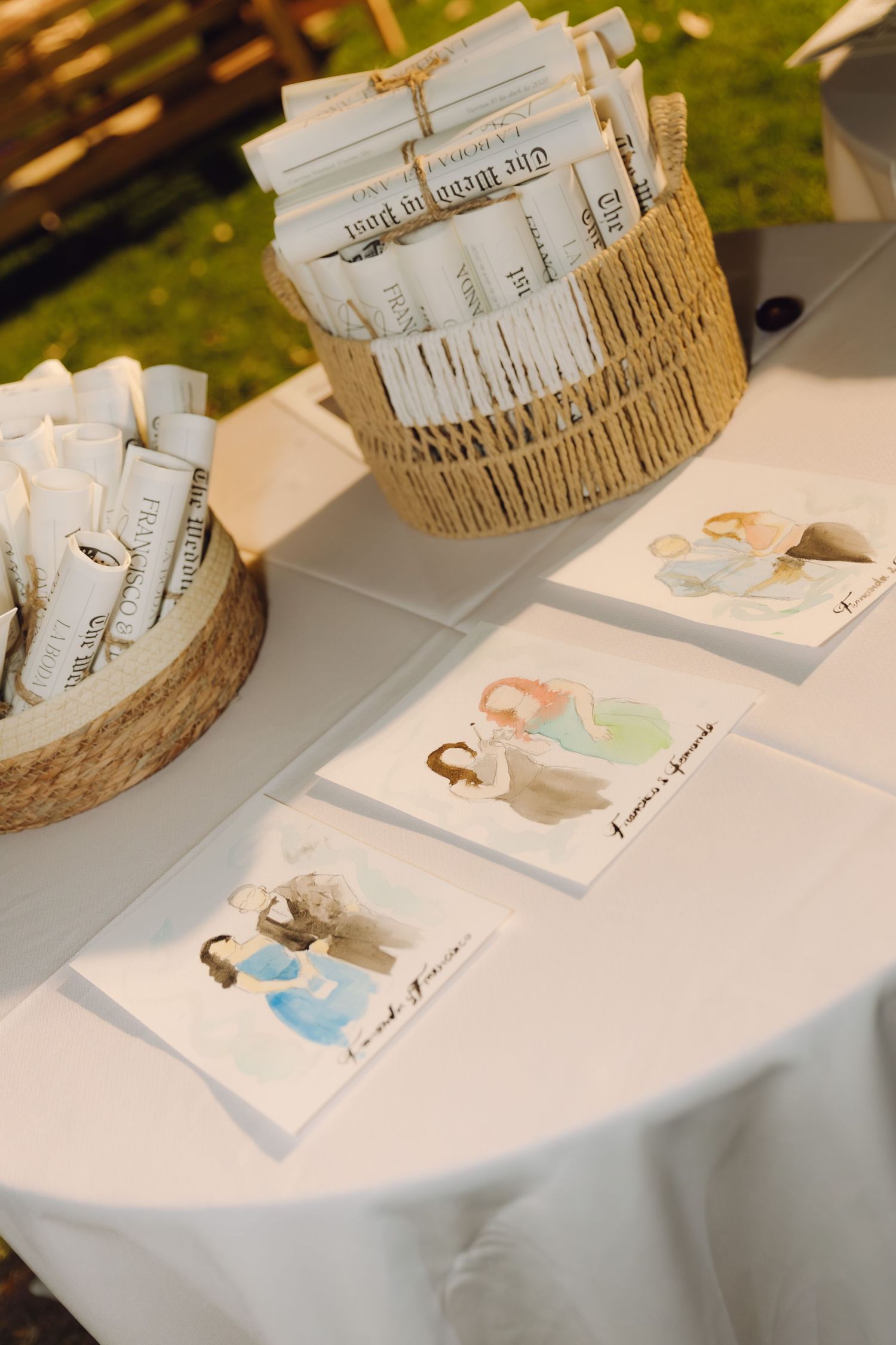 Wedding reception table displaying illustrated programs in wicker baskets with watercolor artwork cards.