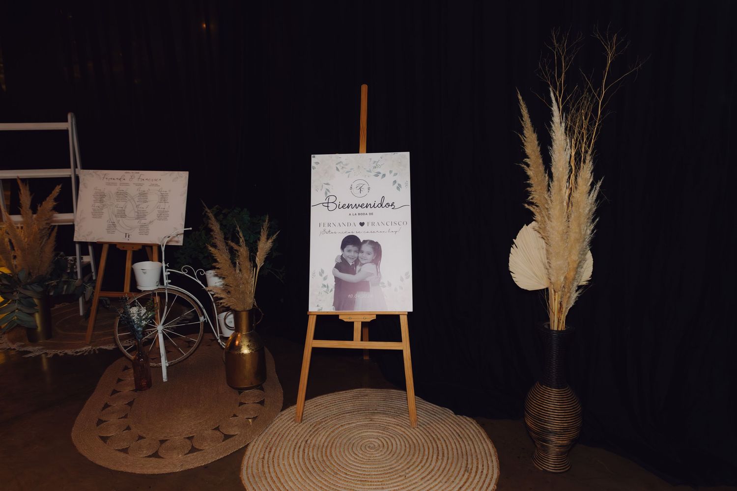 Wedding welcome sign on easel with pampas grass decorations and seating chart displayed at reception.