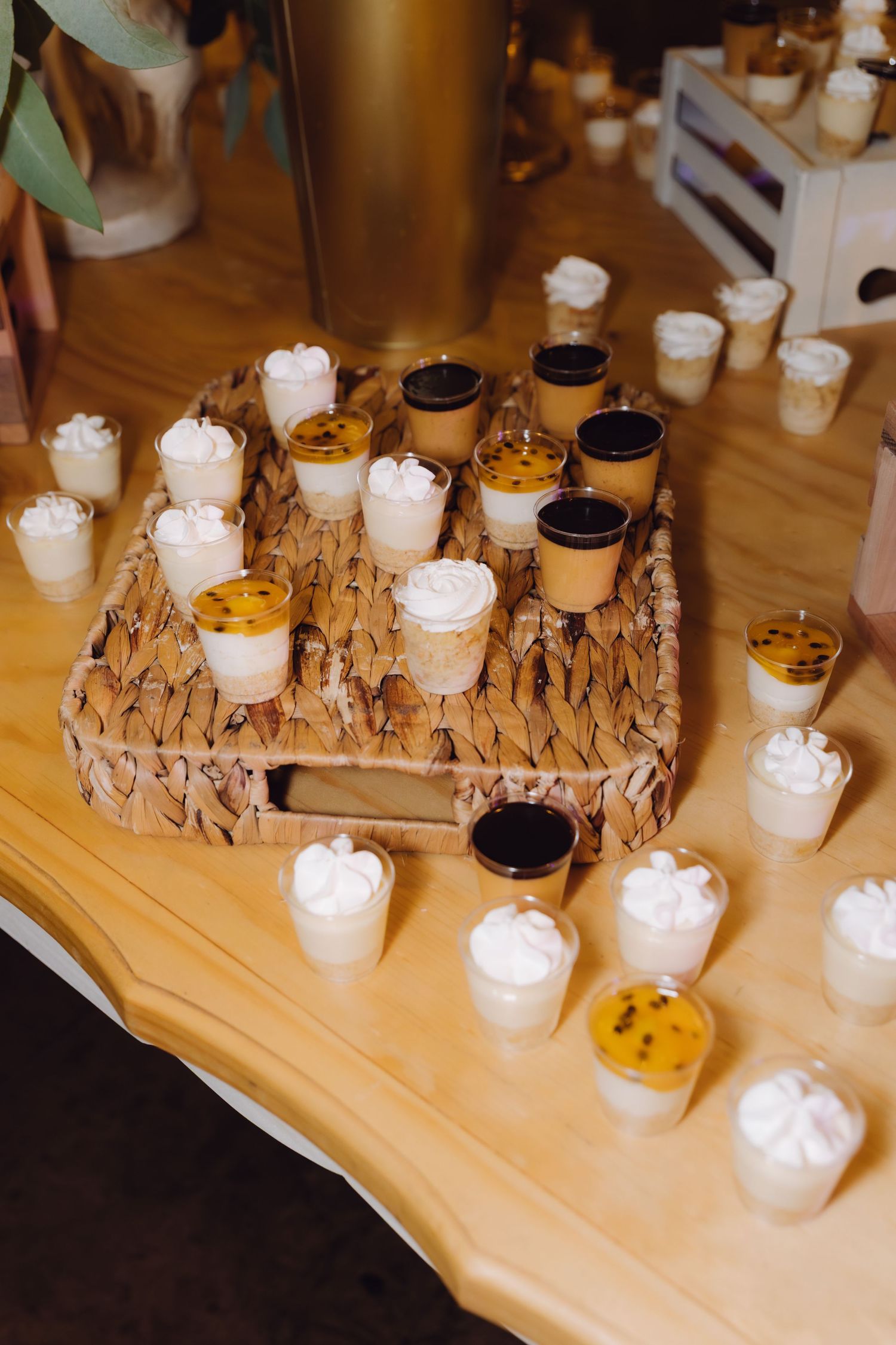 Assorted dessert cups with whipped cream and passion fruit displayed on a woven tray at a wedding reception.