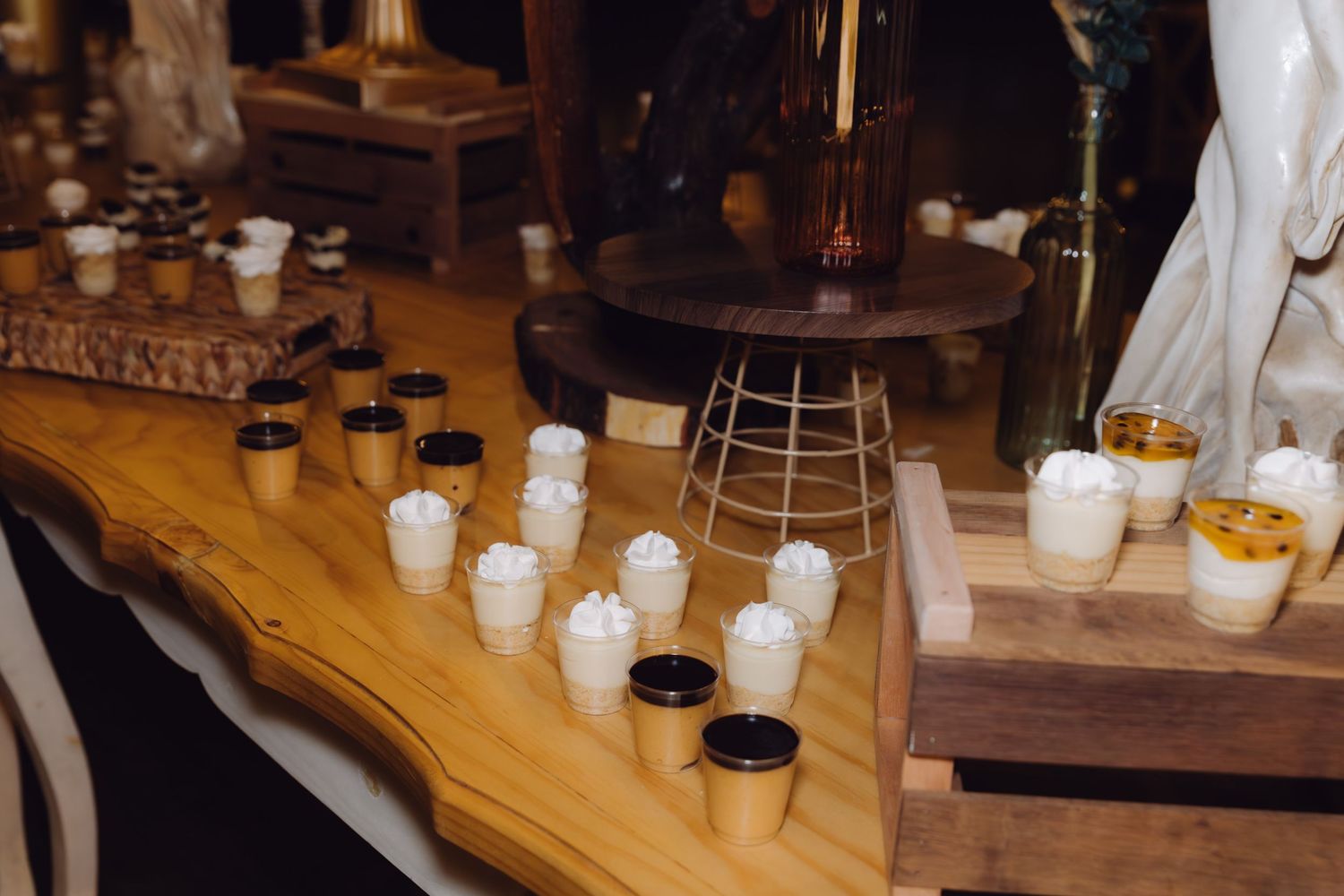 Elegant wedding dessert table featuring mini cups with whipped cream and gold accents on a live edge wood table.