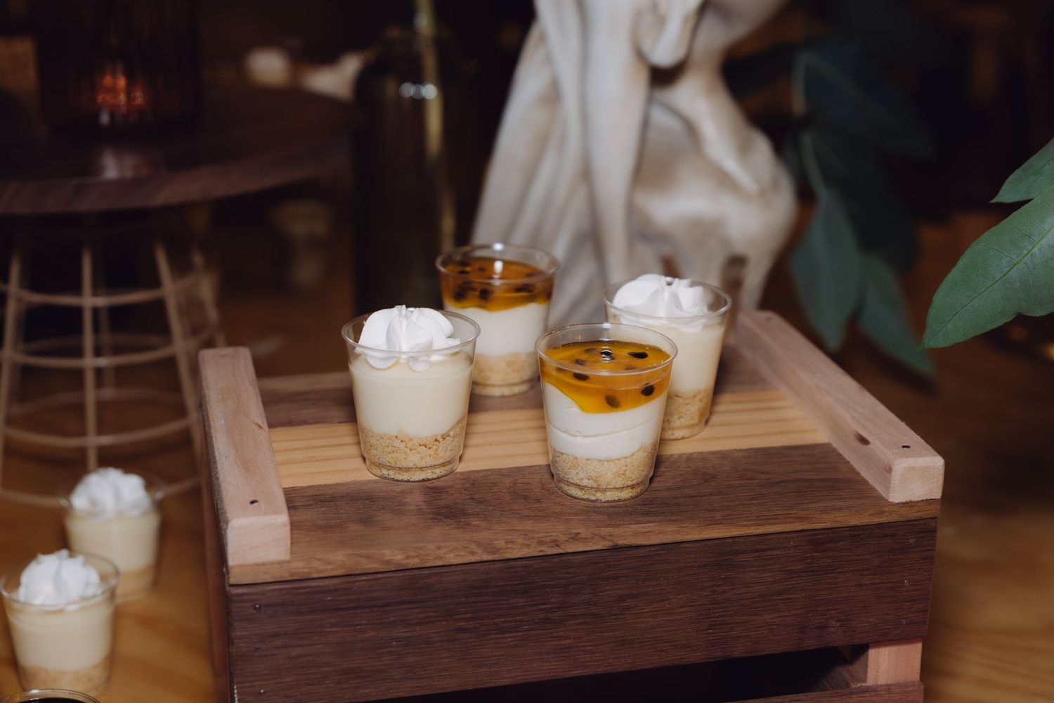 Close-up of layered dessert cups with whipped cream and passion fruit topping on a wooden tray.