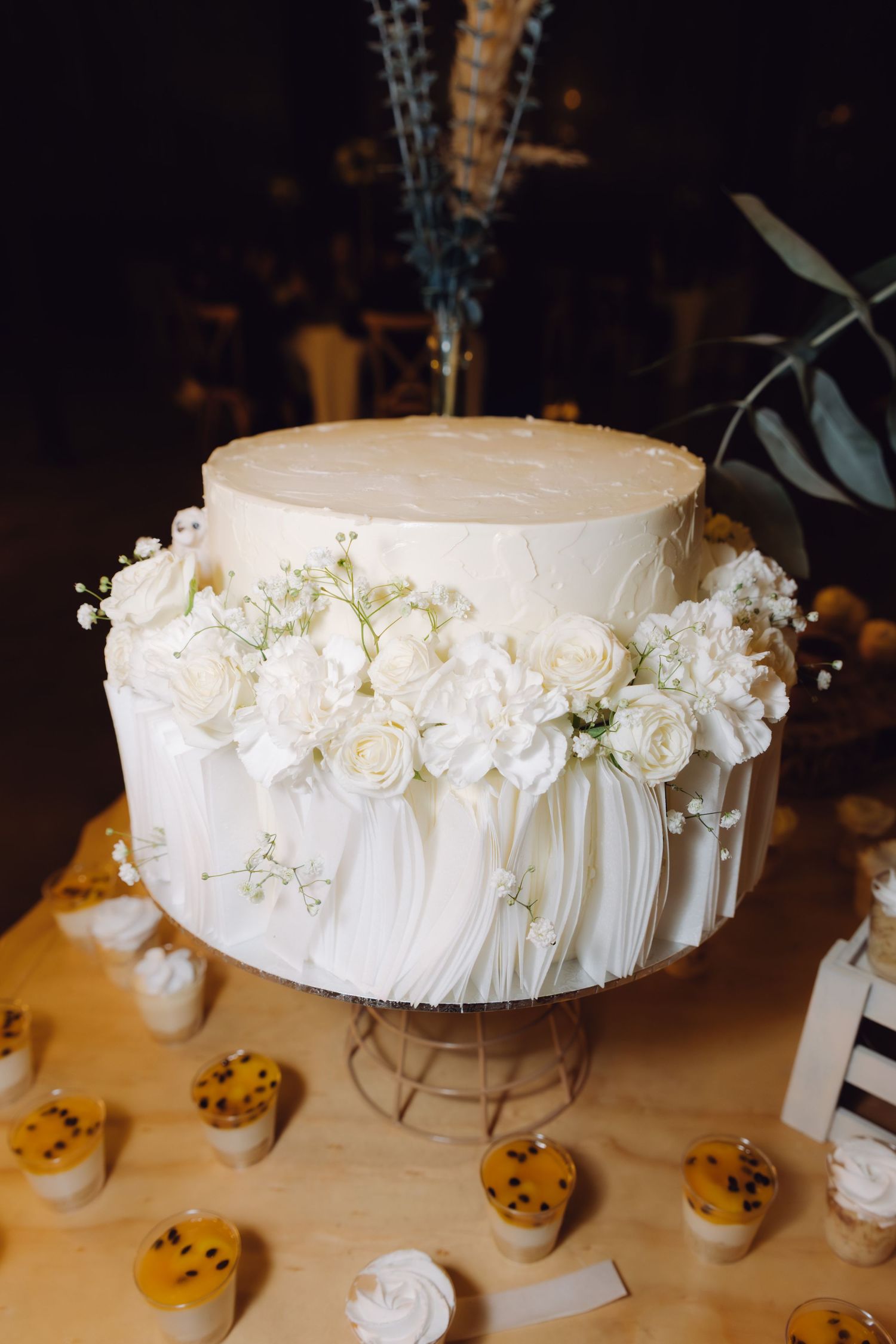 Single-tier white wedding cake decorated with fresh white roses and delicate flowers on a cake stand.