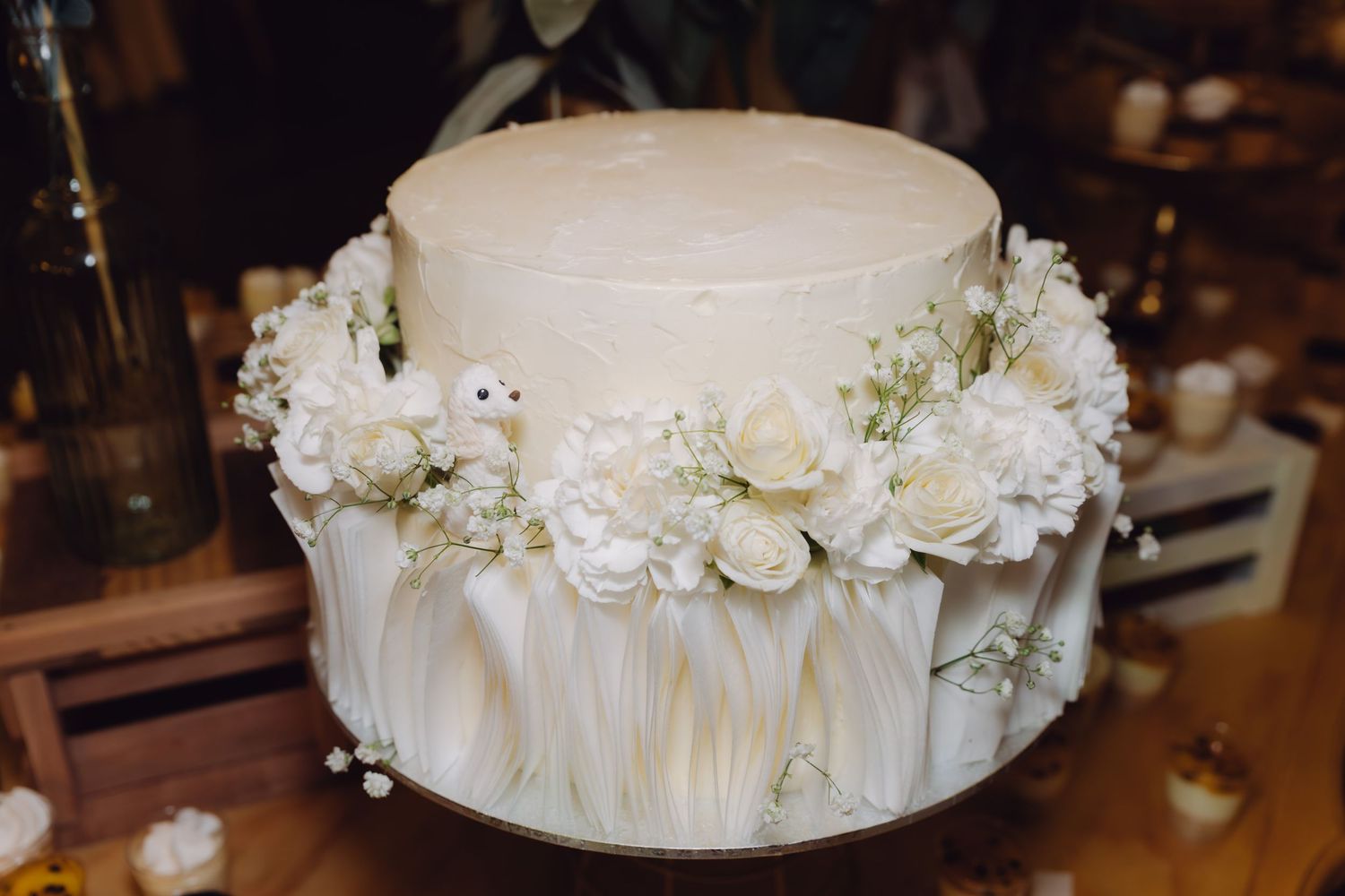 Elegant white wedding cake adorned with fresh white roses and baby breath flowers on a wooden table.