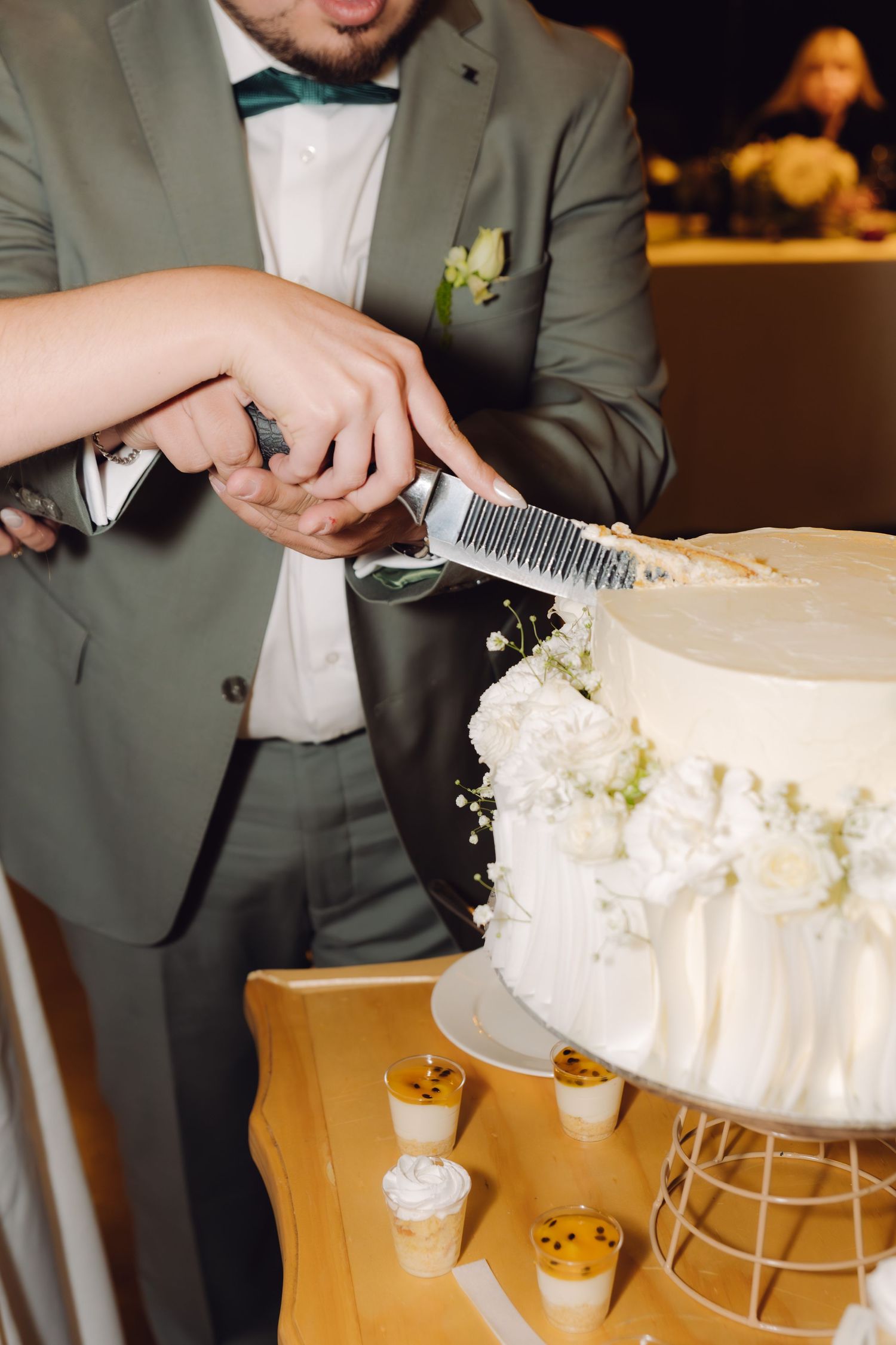 Close-up of bride and groom cutting white floral wedding cake with a decorative cake knife.
