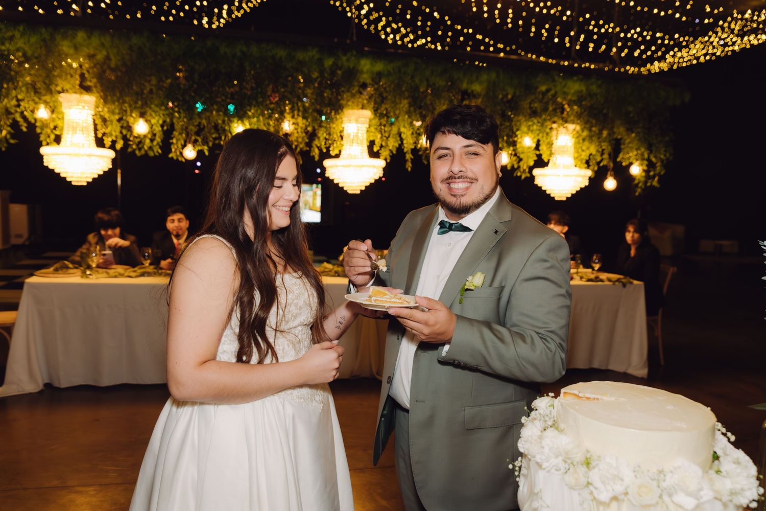 Happy bride and groom smiling while holding wedding cake slices at their beautifully decorated reception.