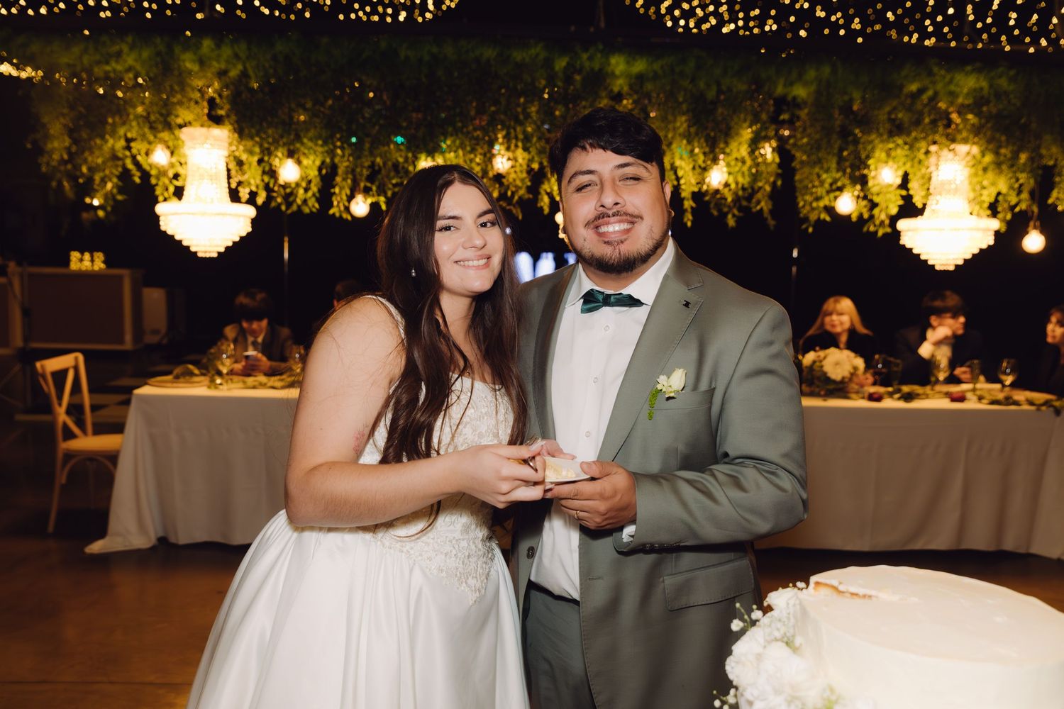 Smiling newlywed couple posing together with wedding cake at their elegant garden reception venue.