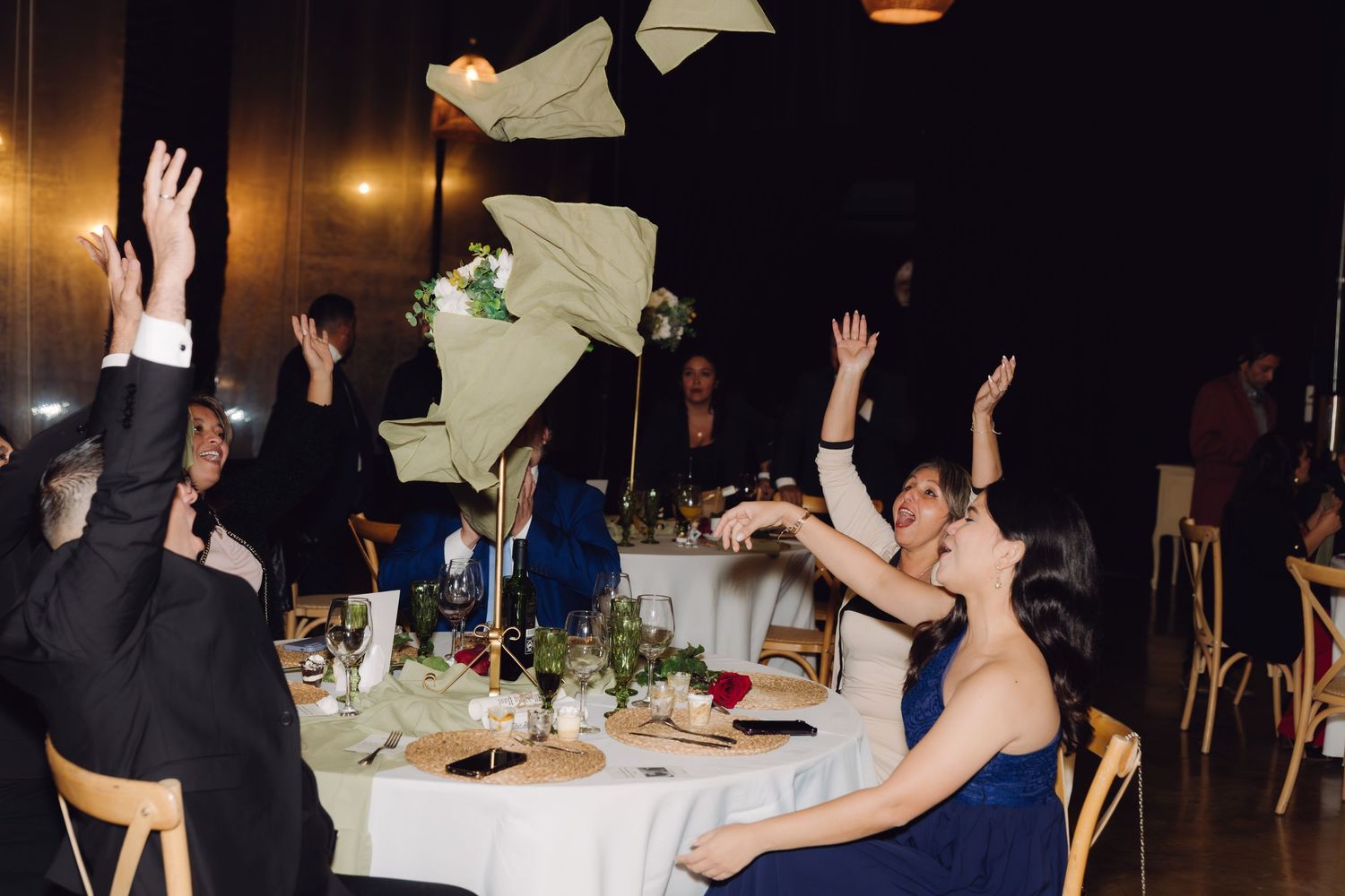 Wedding guests tossing napkins in the air in celebration at an elegantly decorated reception dinner.