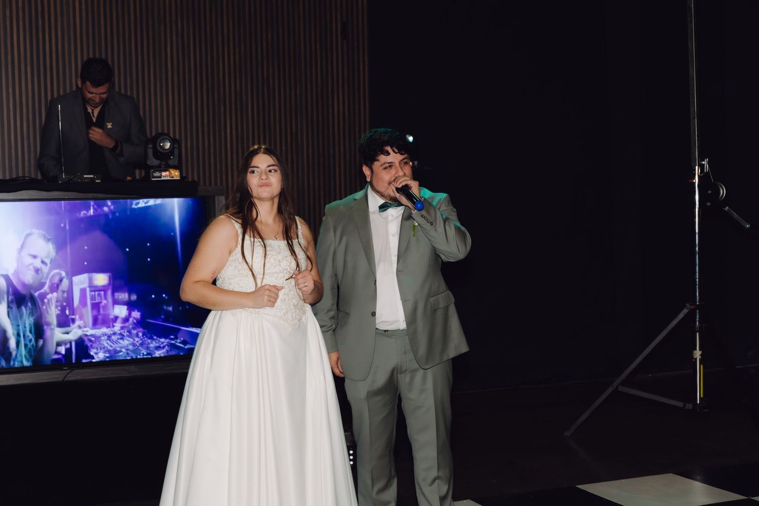 Bride and groom singing together on stage with DJ setup at their wedding reception.