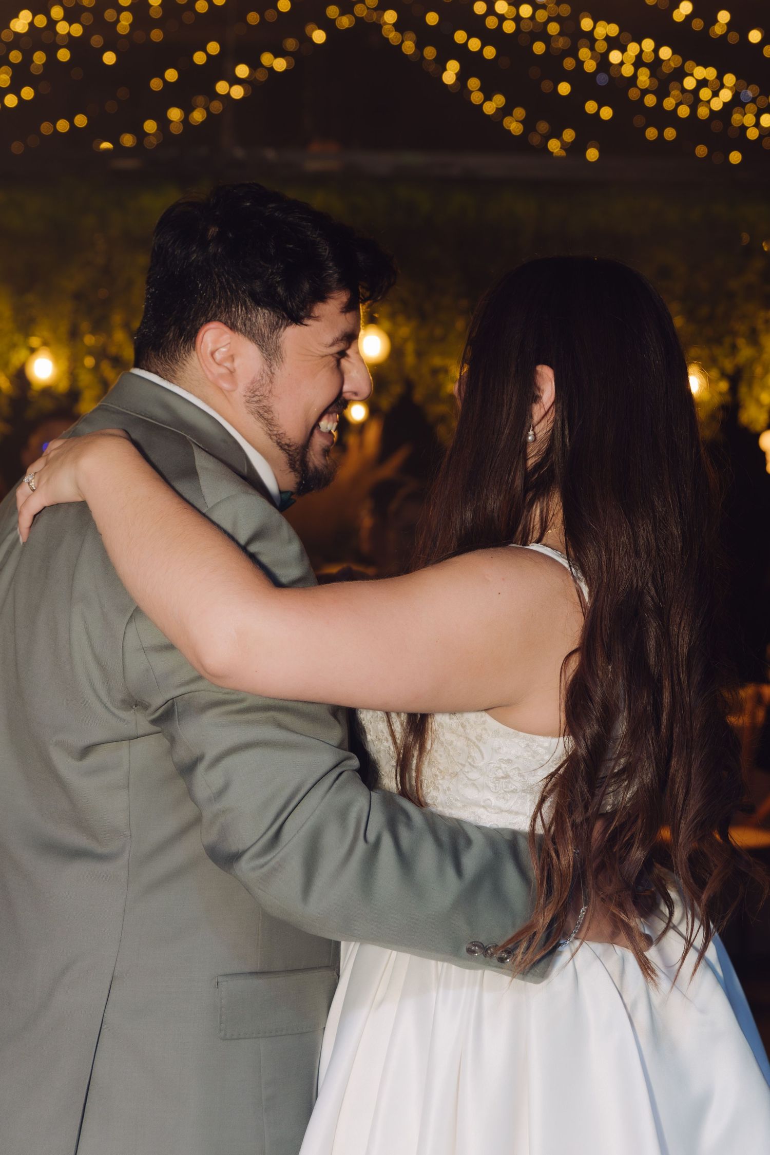 Newlyweds share intimate first dance moment under golden bokeh lights at evening wedding reception.