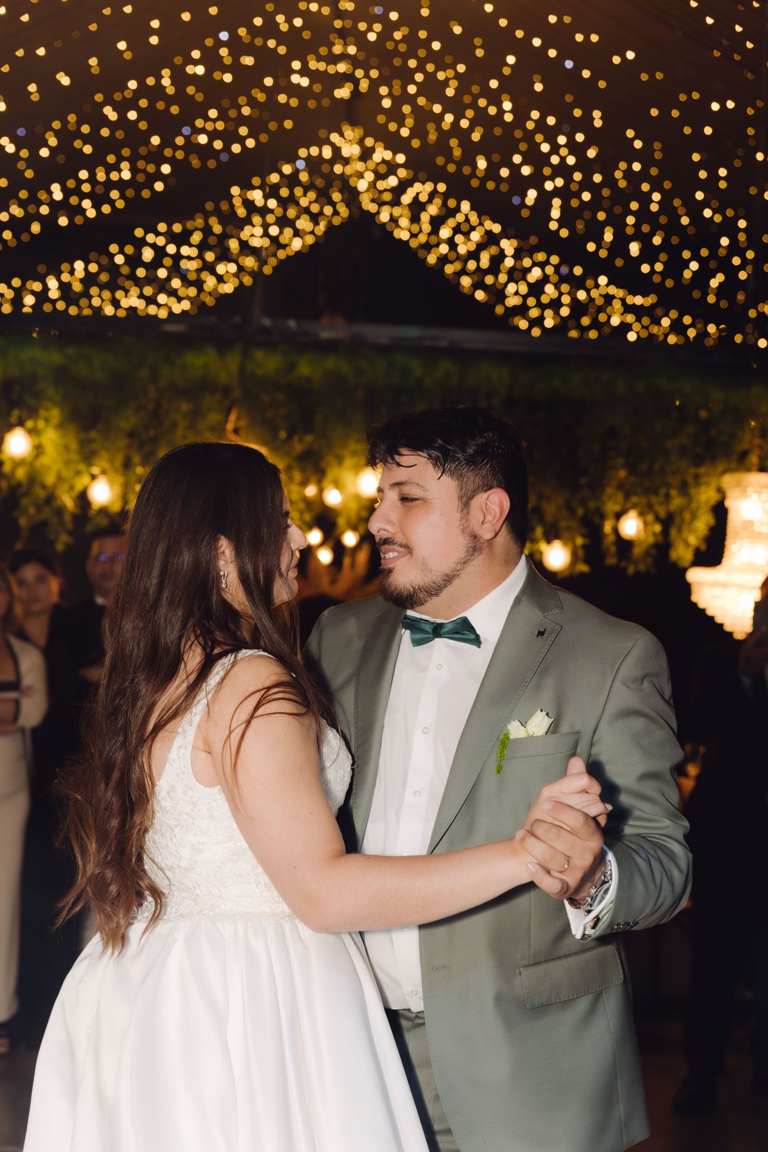 Bride and groom share romantic first dance under warm golden fairy lights at wedding reception.