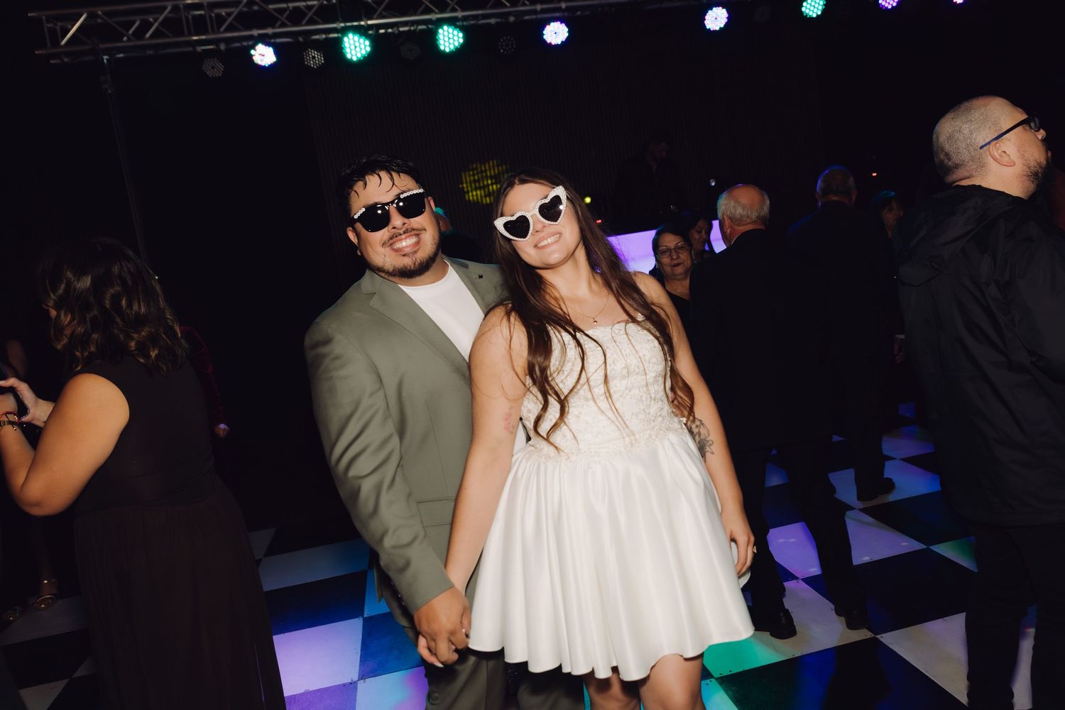 Bride and groom pose on a dance floor wearing fun white sunglasses.